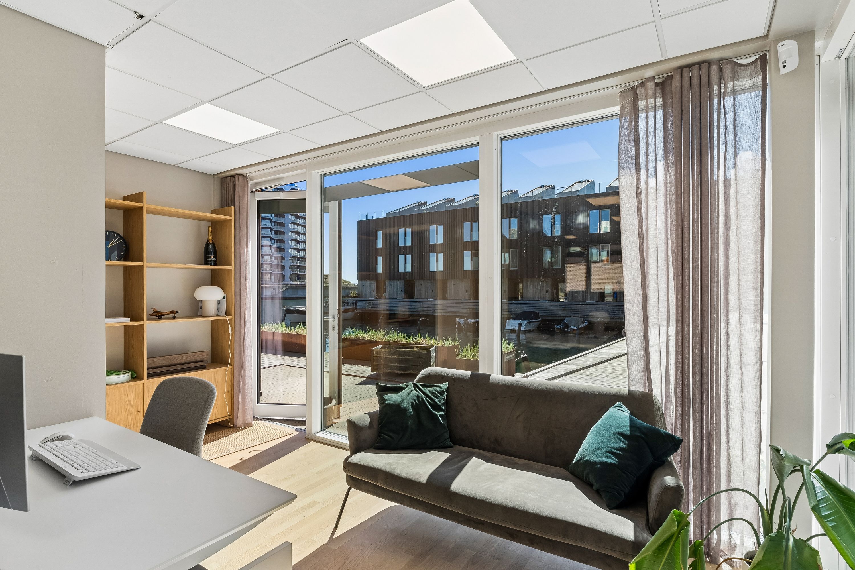 Et kontorlokal med skrivebord og computer og en lænestol samt en sofa med grønne puder og et gulvtæppe