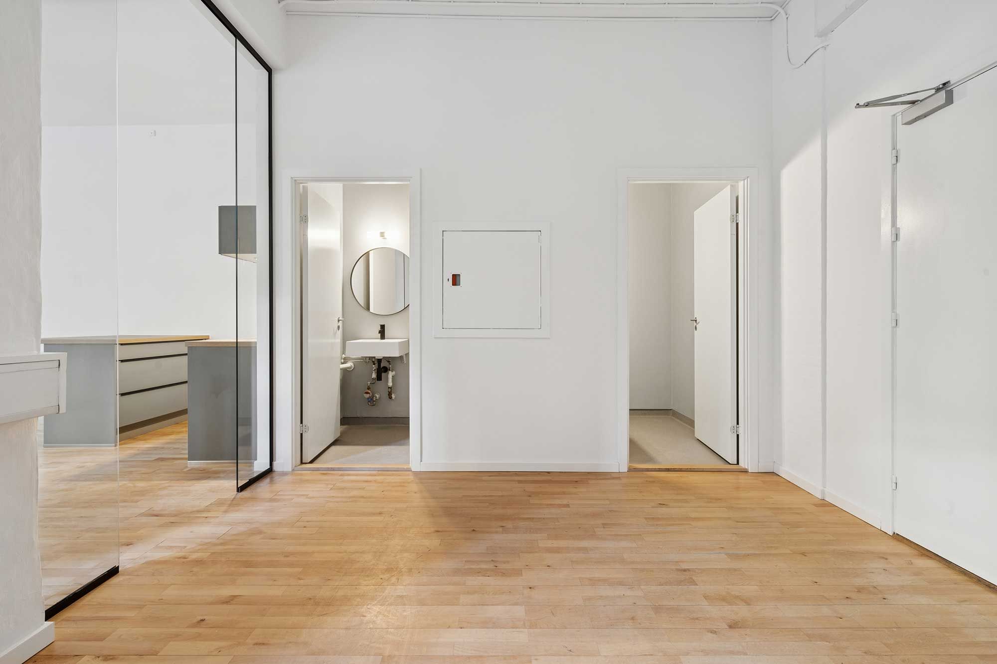Rummelig og lys, nyrenoveret kontorlejlighed med højloft, højkvalitets trægulv og skarpe hjørner. Toiletrum og vaskerum med moderne design. Styrende glasdør til et andet rum.