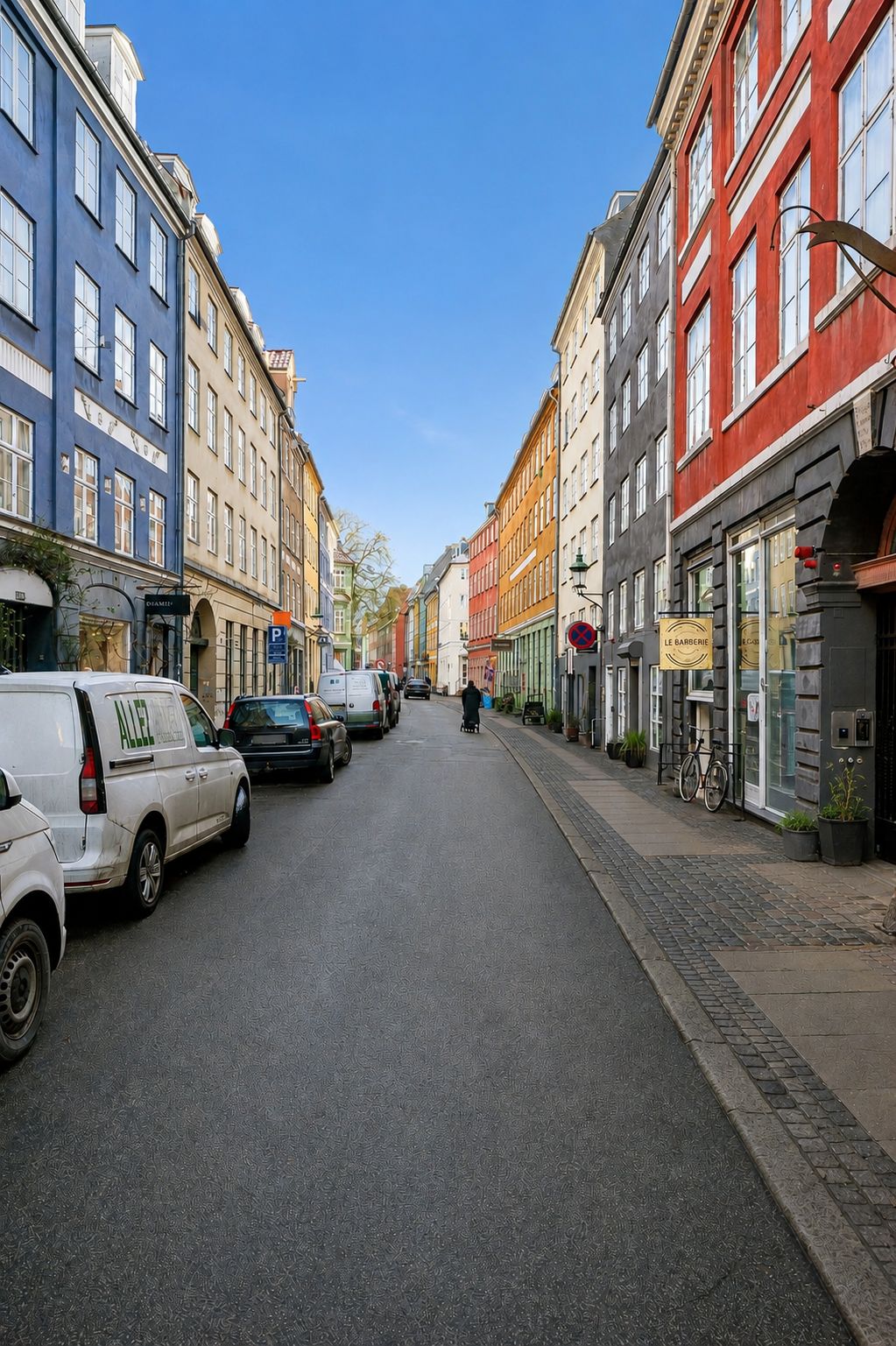 To hvide og to røde lastvogne parkeret på en tomgangsvej med røde og blå bygninger og et menneske, der går på fortovet med en cykel