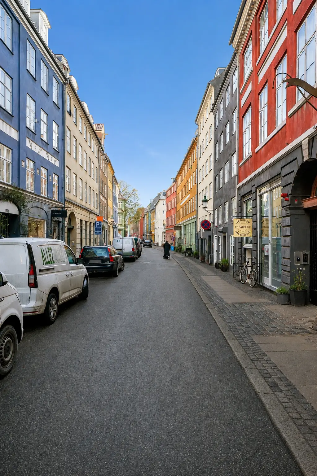 To hvide og to røde lastvogne parkeret på en tomgangsvej med røde og blå bygninger og et menneske, der går på fortovet med en cykel