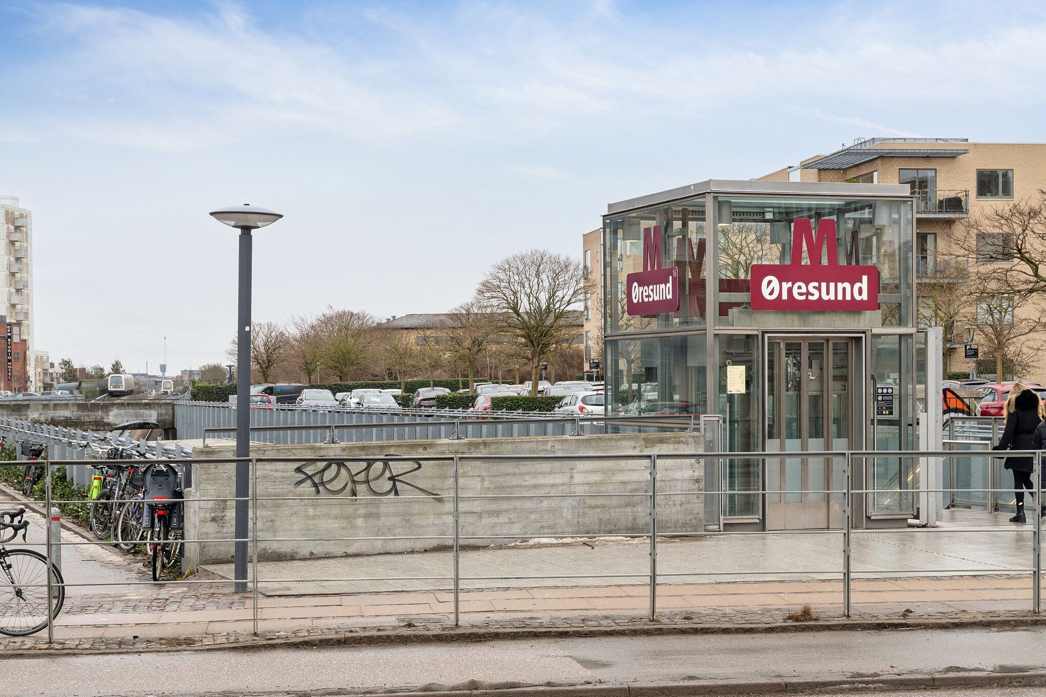 Ved hovedindgang til Øresund metrostation står en cykel op til en parkeringsstang med flere cykler og en vognparkeret i baggrunden
