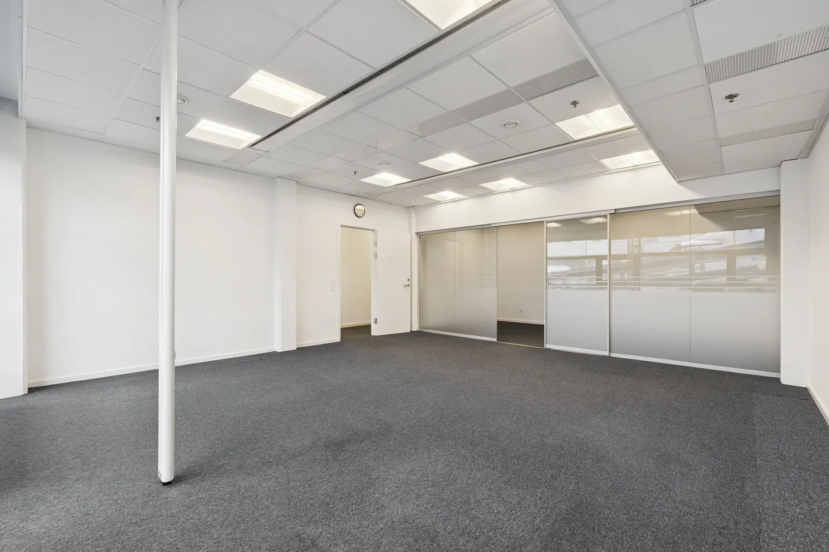 En stor, velplejet lagerhal med hvide vægge og gulv, glasdøre, hvide lofter, indbyggede lysekroner og en hvid søjle. Et hvidt vægur med ure.