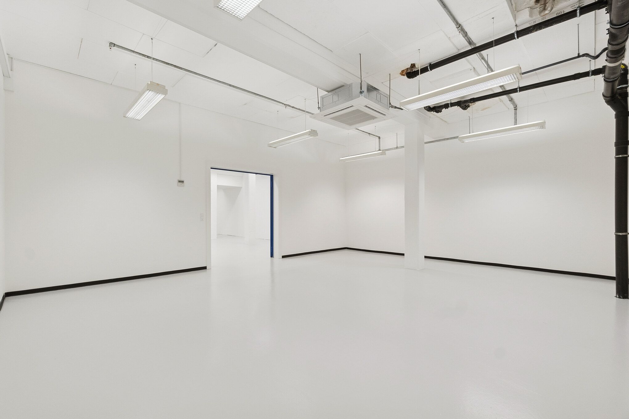 Rummelig industrihal med hvide vægge, lyse armaturer og ren gulvoverflade, ideelle til lager og showroom, med højt til loftet og moderne ventilationssystemer