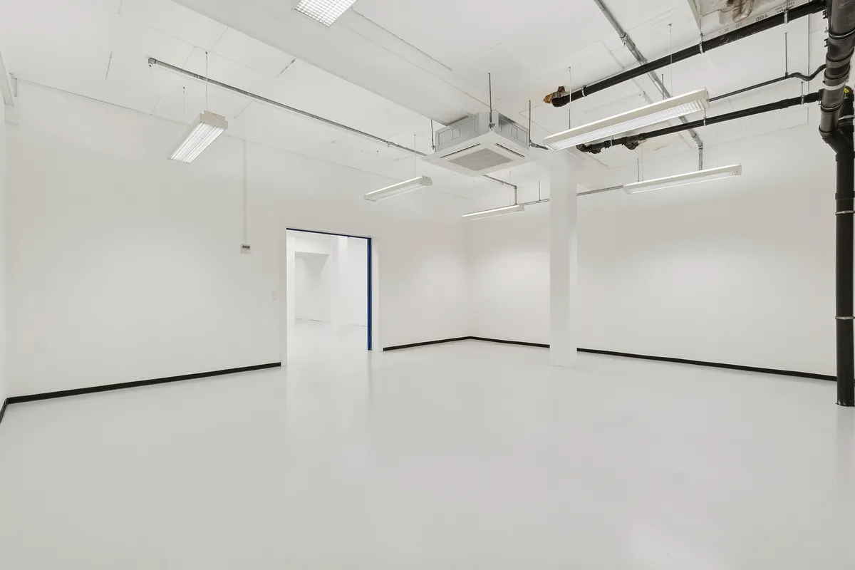 Rummelig industrihal med hvide vægge, lyse armaturer og ren gulvoverflade, ideelle til lager og showroom, med højt til loftet og moderne ventilationssystemer