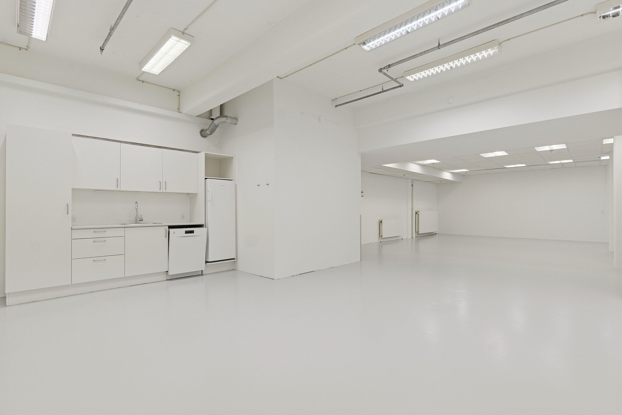 Rent og lyst lager med moderne møbler, hvidt loft og hvide vægge, fuldt udstyret med en køleskab og en vaskemaskine, samt et moderne sømløst gulv