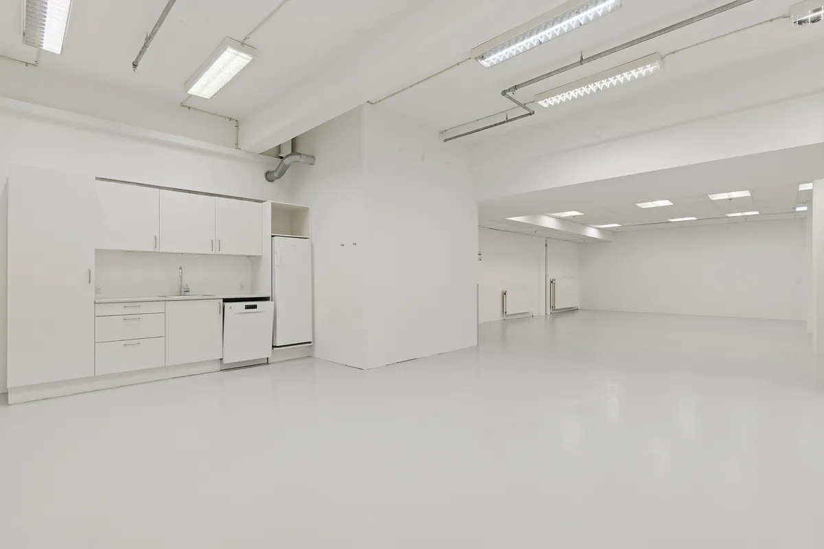 Rent og lyst lager med moderne møbler, hvidt loft og hvide vægge, fuldt udstyret med en køleskab og en vaskemaskine, samt et moderne sømløst gulv