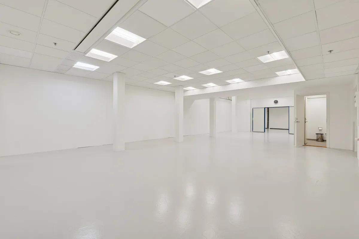 Et rummeligt, hvidt lejerum med blanke vægge og loft og fire hvide søjler. Rummet har to åbne døre og en toiletdør med håndklædeholder og papirkurv. Loftet er forsynet med flere hvide lyskatler