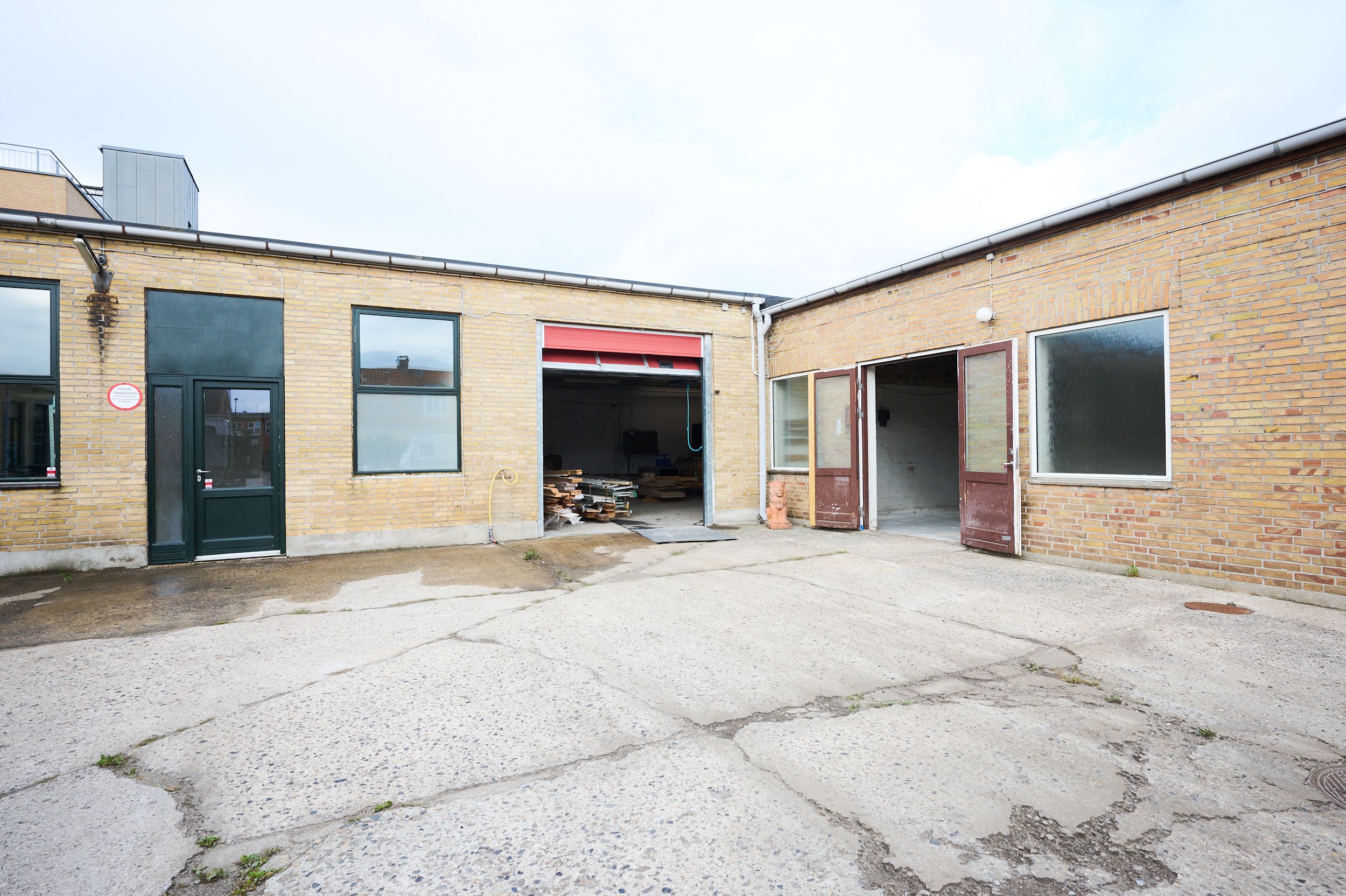 Et toetaget bygning med røde mursten og glasvinduer. Garagedøre er åbne og en røgfangere på taget. Et rødt banner er hængt på den ene garage.