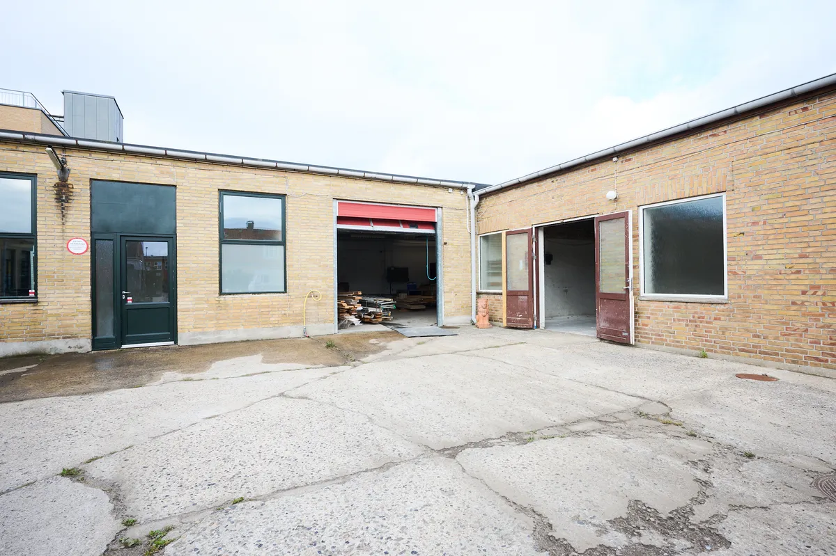 Et toetaget bygning med røde mursten og glasvinduer. Garagedøre er åbne og en røgfangere på taget. Et rødt banner er hængt på den ene garage.