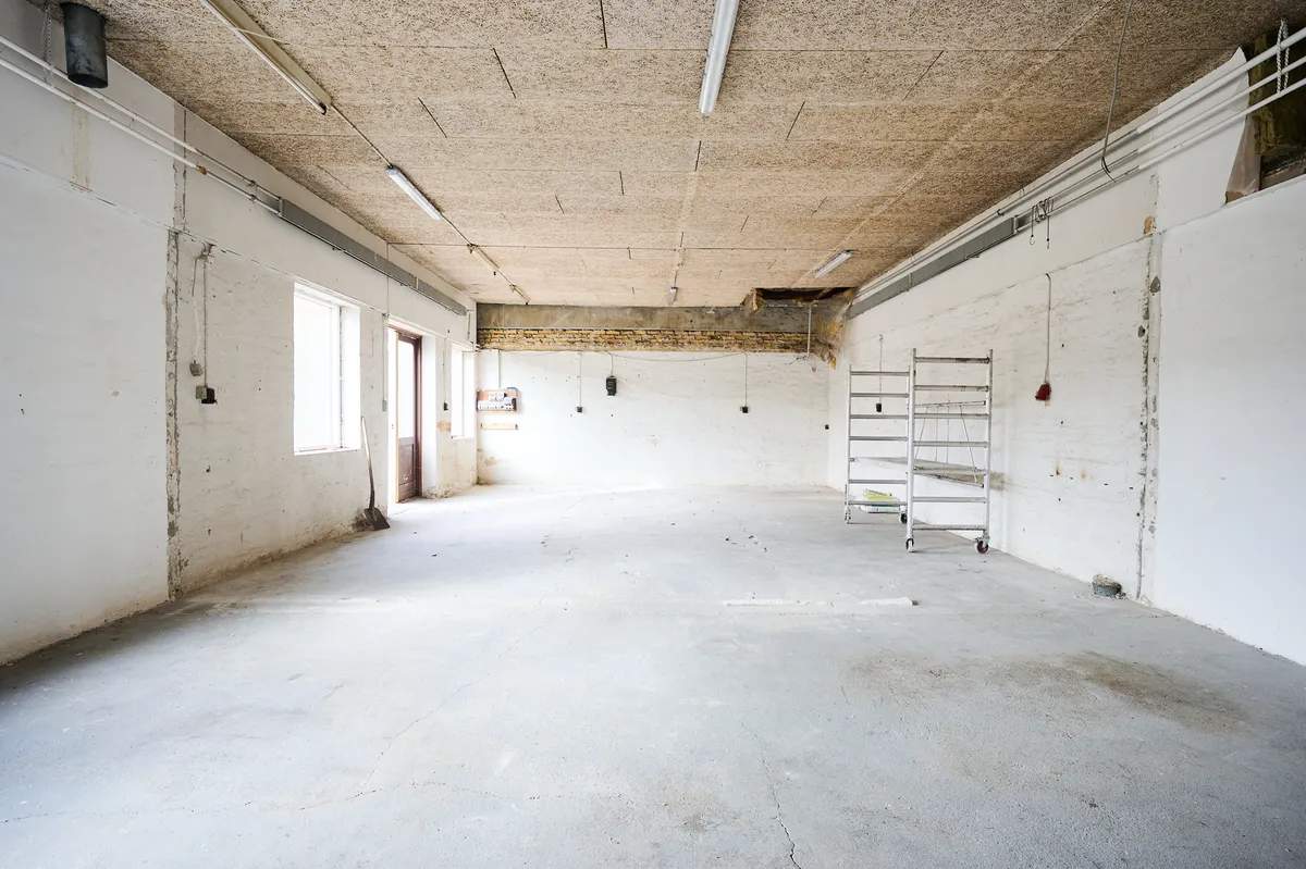 Produktionslokaler med lyse lofter og hvide vægge, stige og tomme vinduer i baggrunden