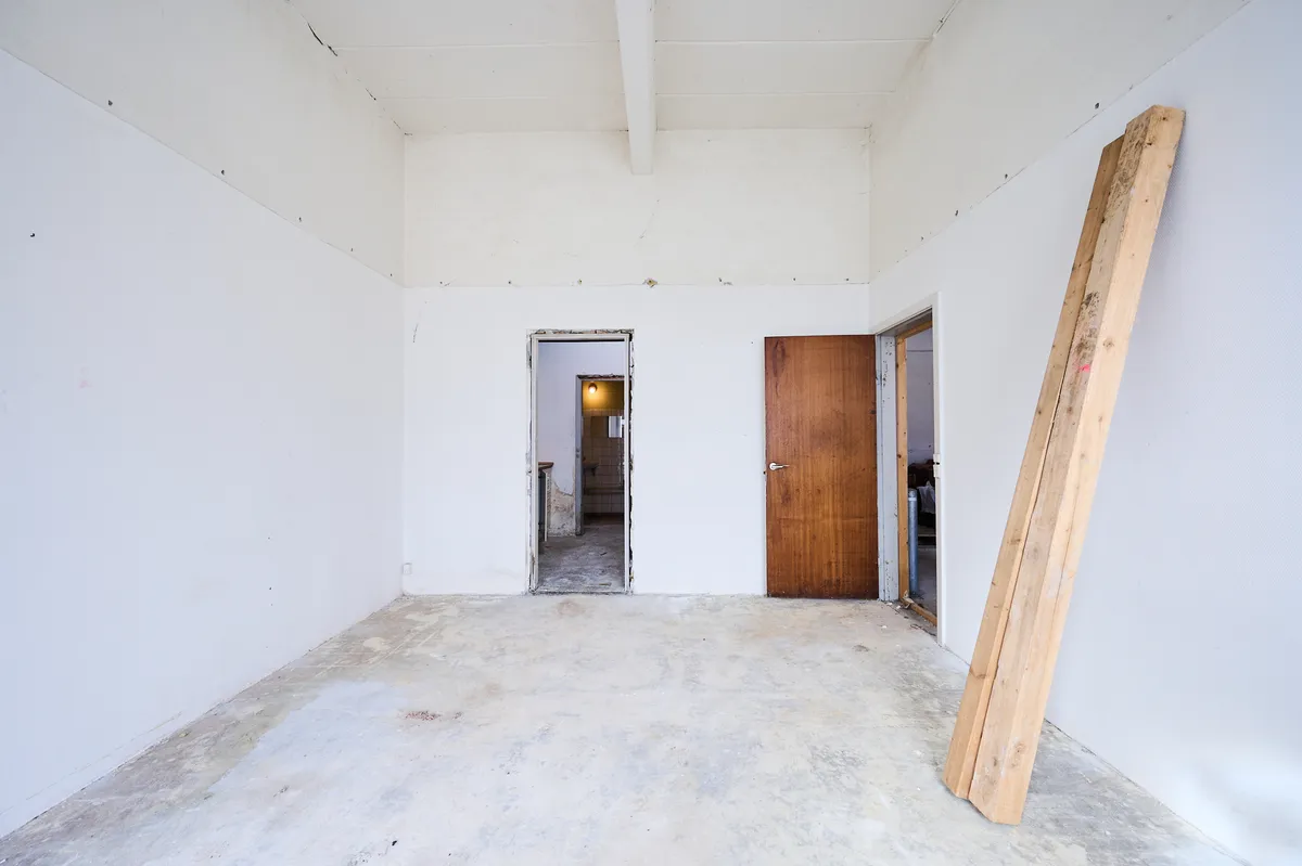 En stor og tom rum med hvide vægge og to åbne døre og en lang bjælke mod højre side