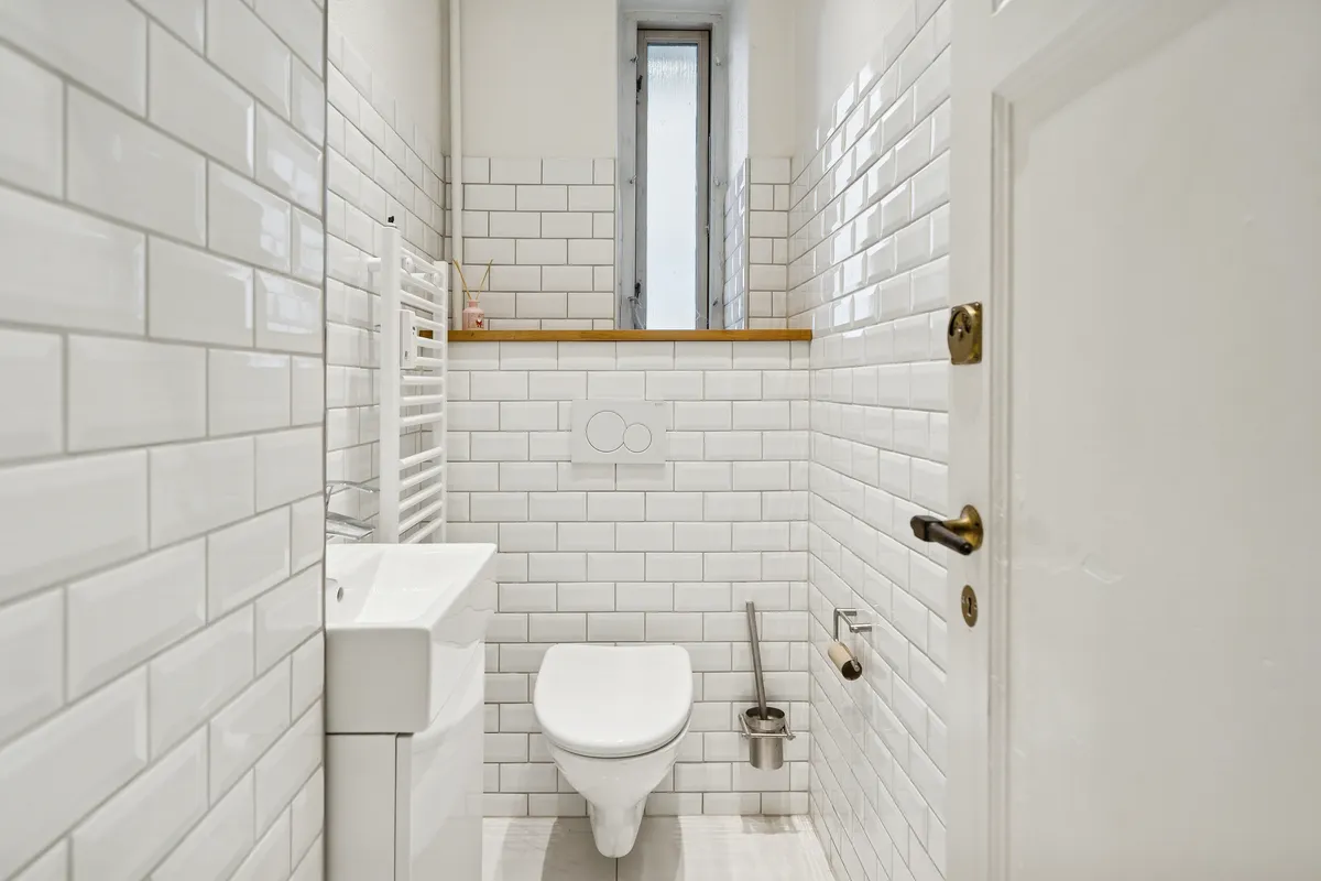 Moderne toiletrum med hvide fliser og lyse møbler. Toilettet med åbne toiletbriller og lukket dør. Hvidt vask og tørretumbler i hjørnet