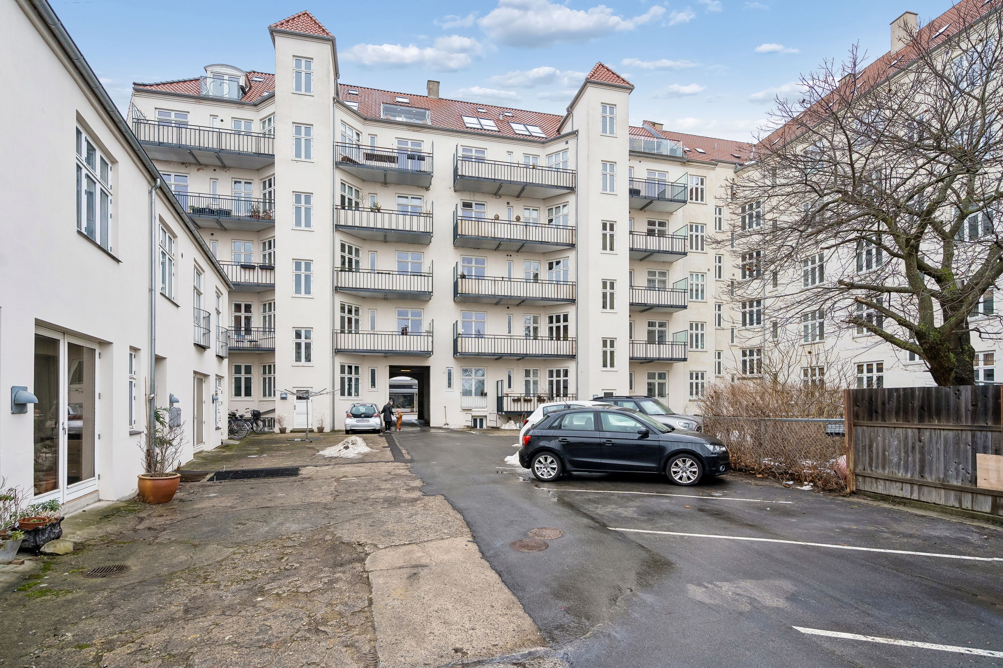 Mange biler parkeret på en parkeringsplads med biler parkeret på begge sider og en person, der går ud af en garage.