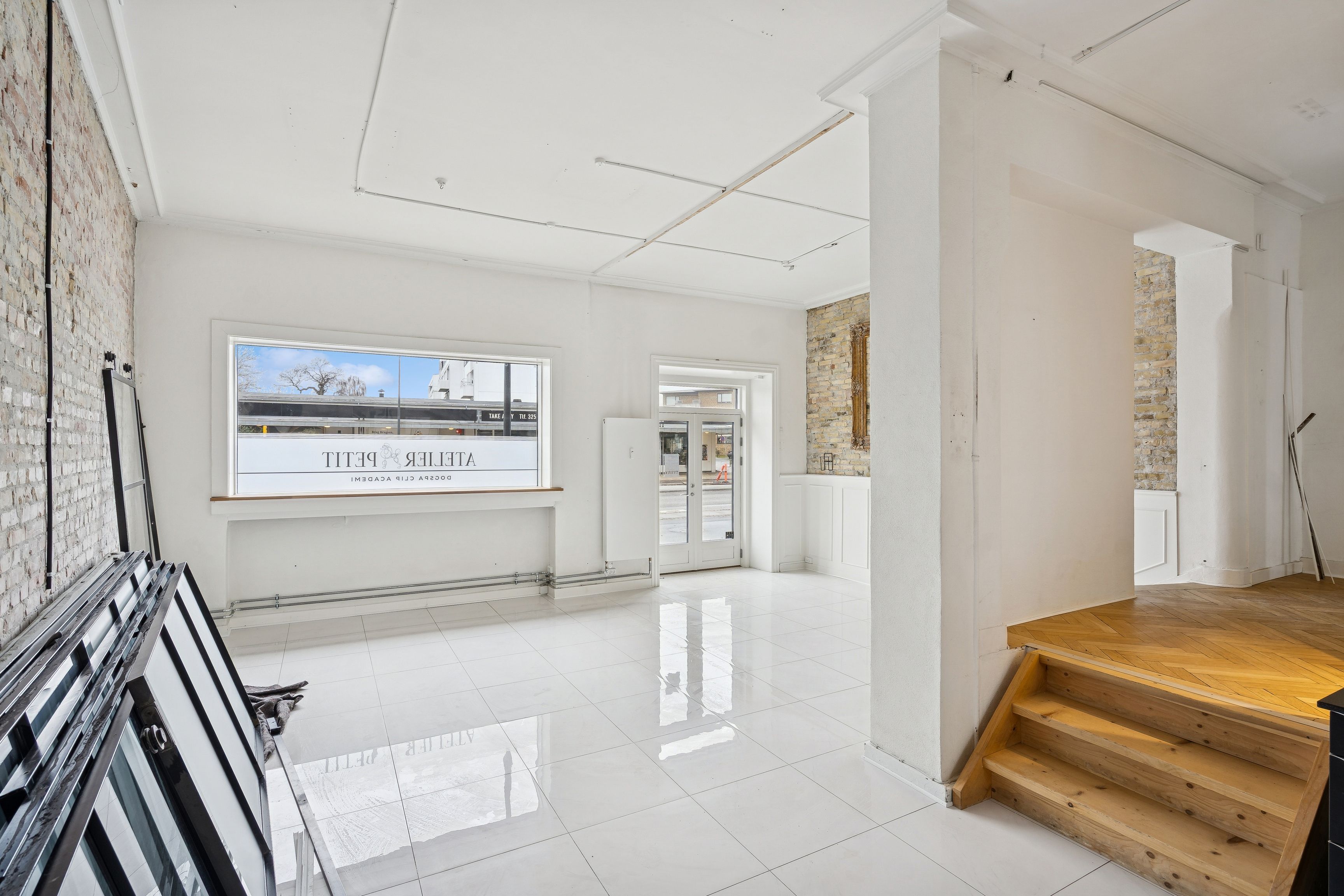 Rummelig kontorflise med hvide vægge og blanke gulve samt store vinduer med glasruder og et mærke på en af dem