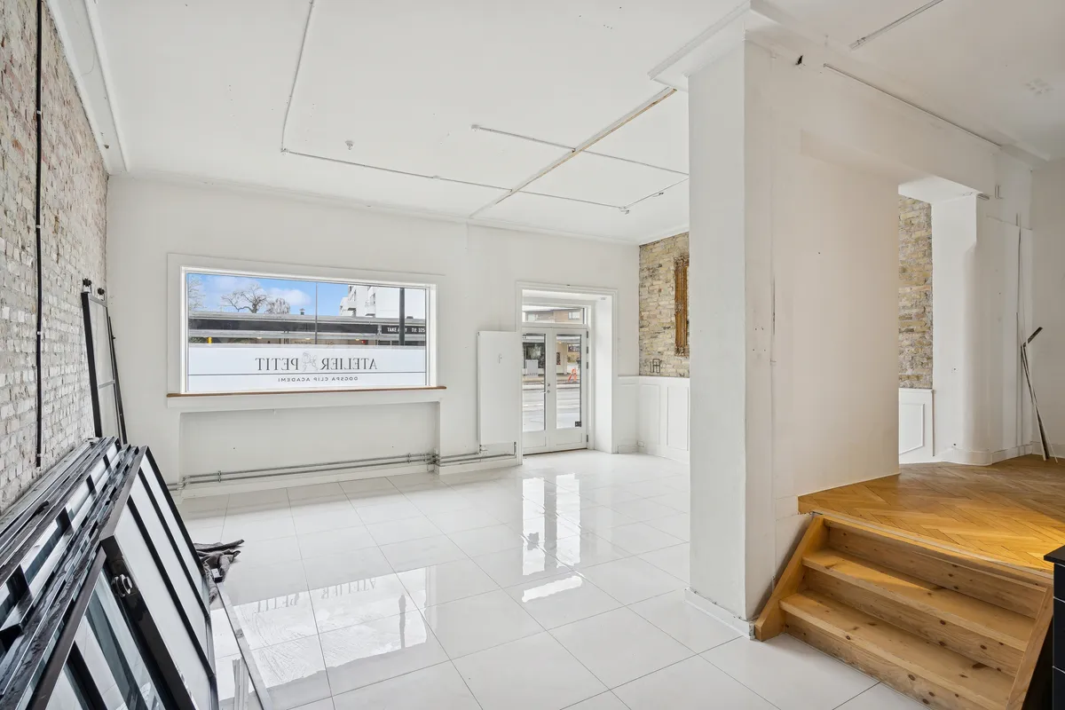 Rummelig kontorflise med hvide vægge og blanke gulve samt store vinduer med glasruder og et mærke på en af dem