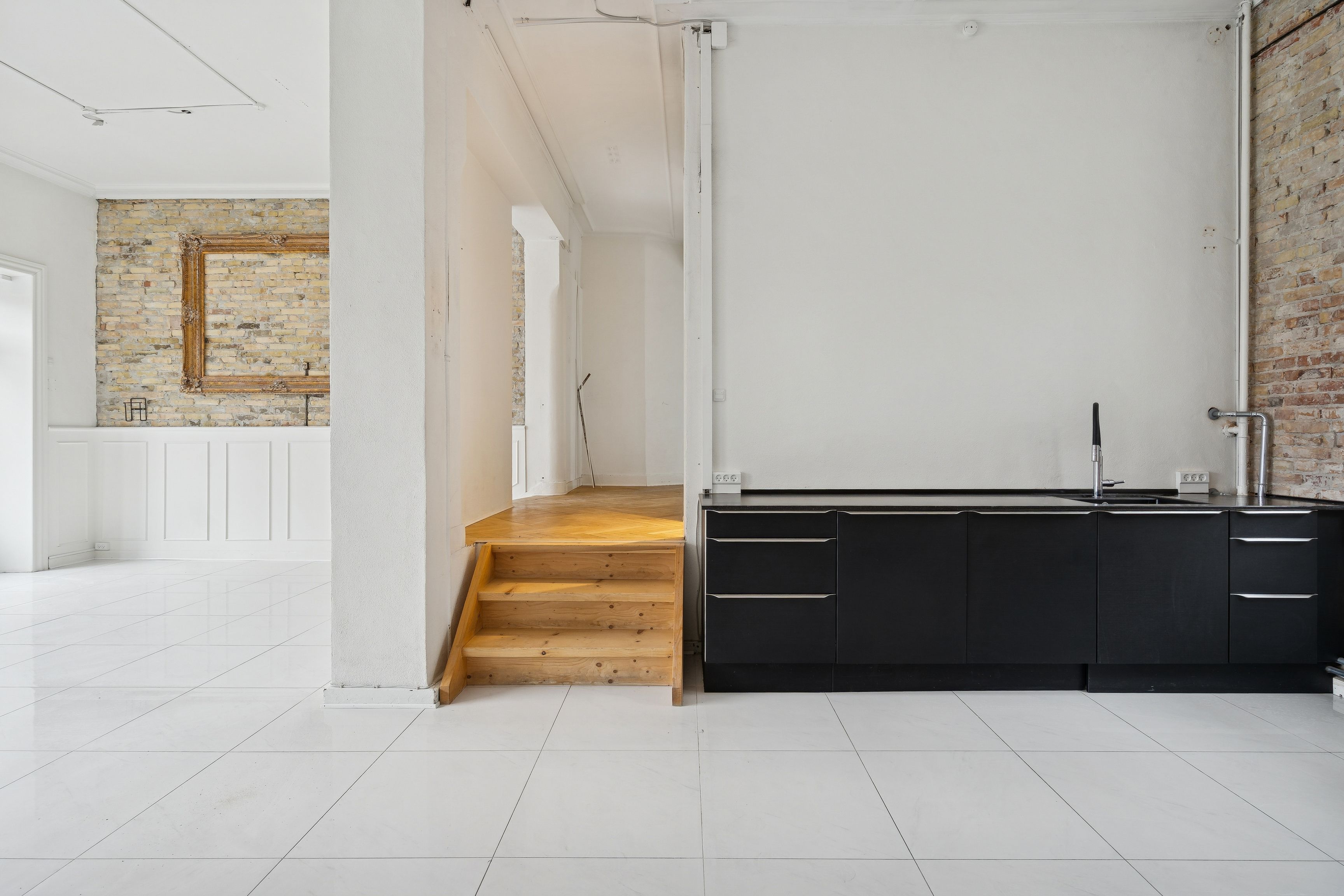 Minimalistisk indretning med hvidt loft og vægge, lysegul trætrappe og mørke, pudsede skabe med køkkenhøj og lysegrå, rektangulært gulv