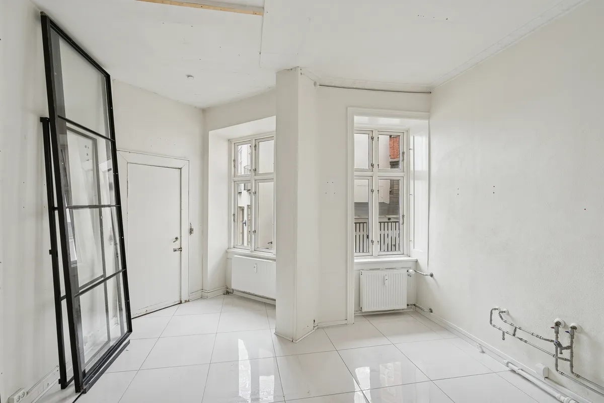 En tom og lys stue med hvide vægge, gulve og loft, samt to vinduer med store glasruder