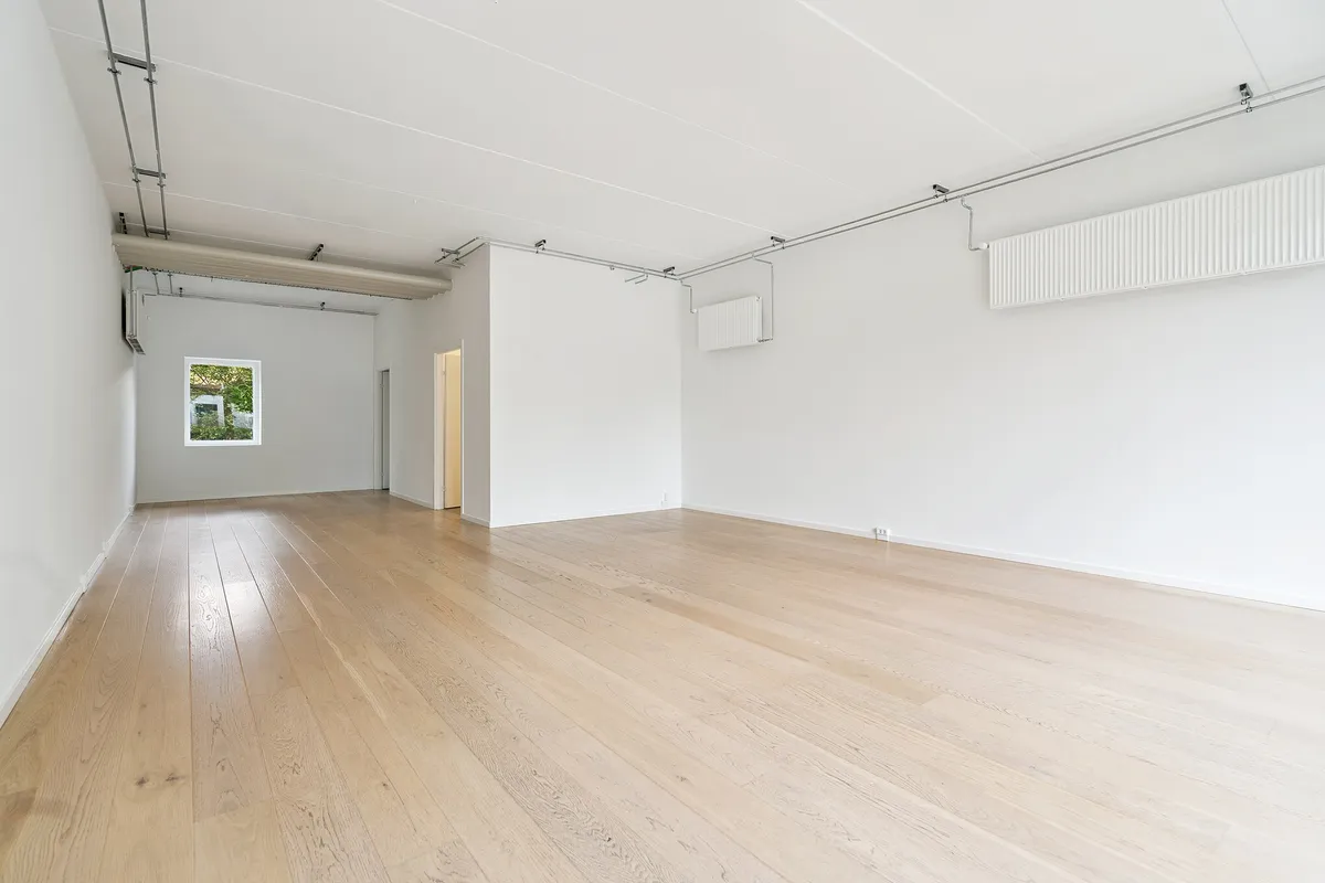 En tom og hvidmalet lokale med trægulv og et lille vindue i en af væggene