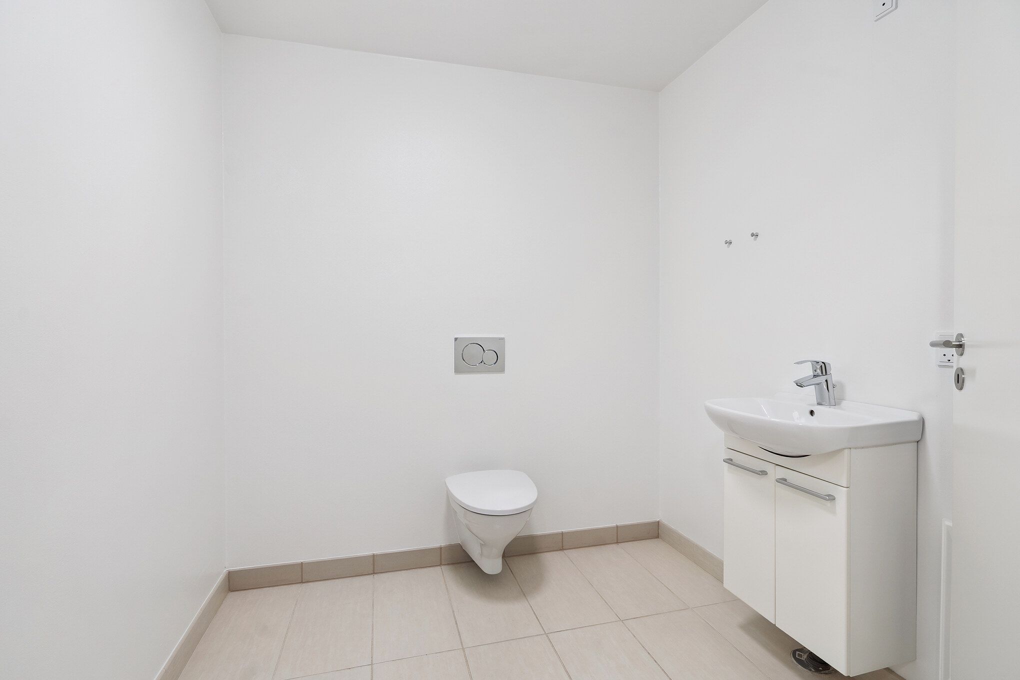 En hvid og pæn toile med toiletpapirholder og håndvask i hvidt og beige interiør med gulvtæppe