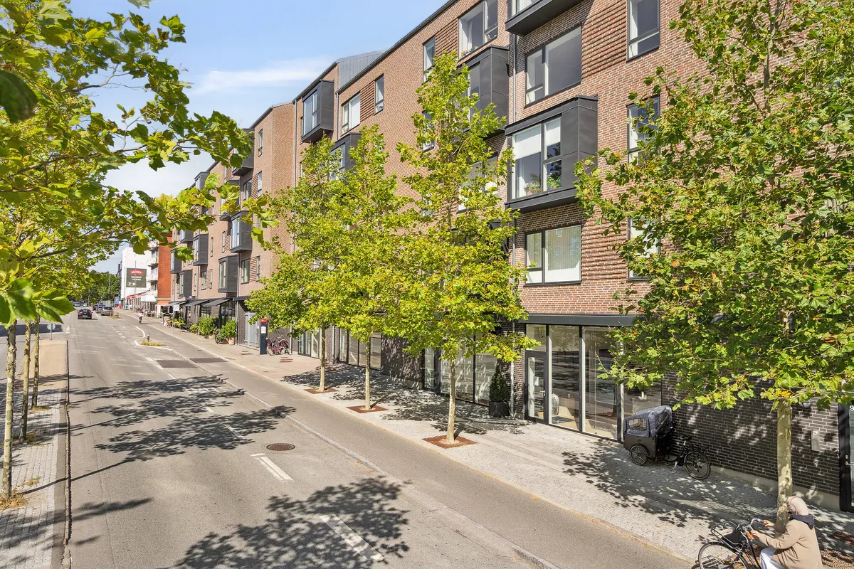 En gågade med nye huse, hvor kvinder cykler og gå ned ad gaden med blomstrende træer og røde mursten.