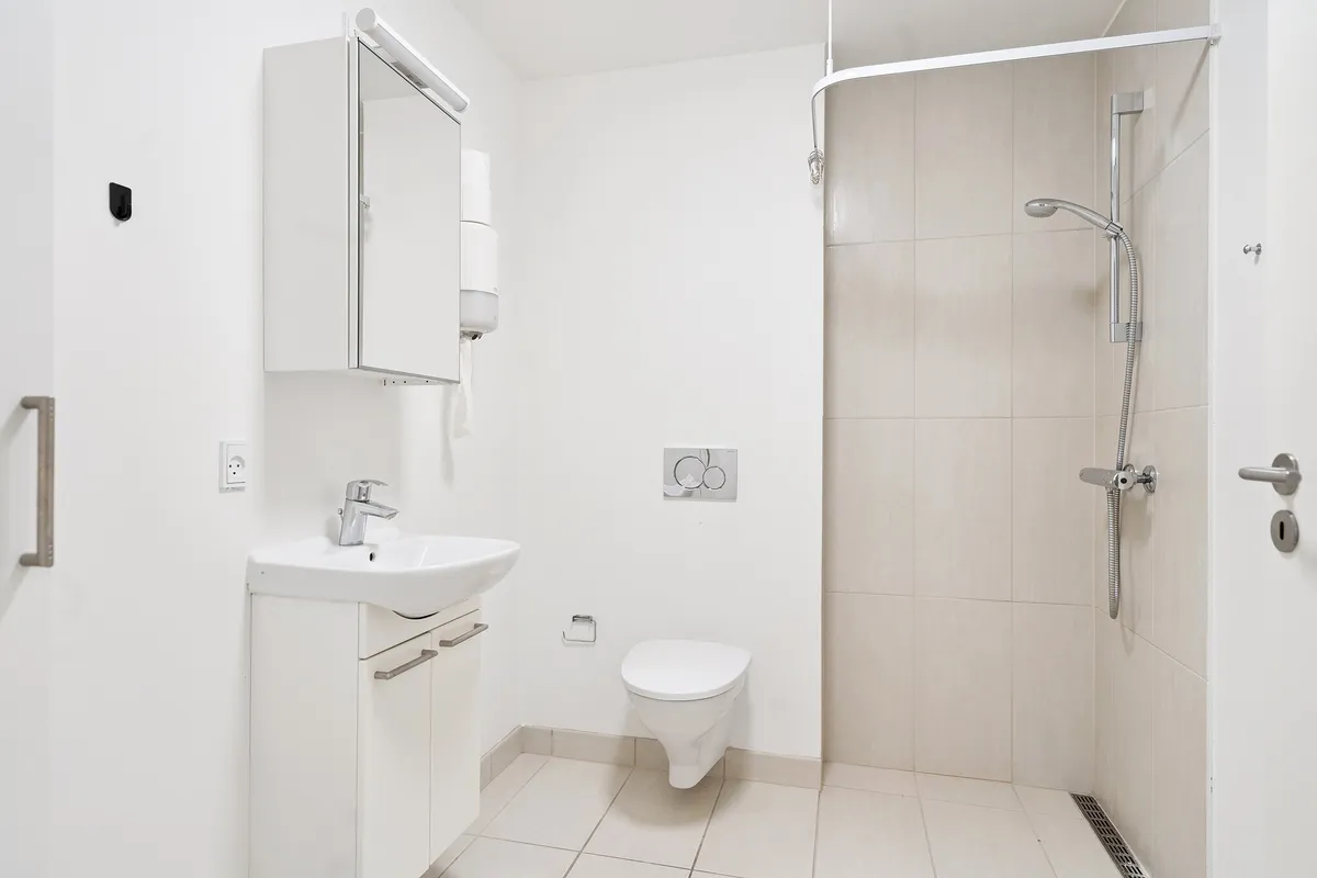 Et minimalistisk, hvidt badeværelse med høj kvalitet og funktionel design. Et moderne toilet med en hvid keramik og en håndvask med integreret håndklædeholder. En moderne brusekabine med en vandhane og en håndklædeholder.