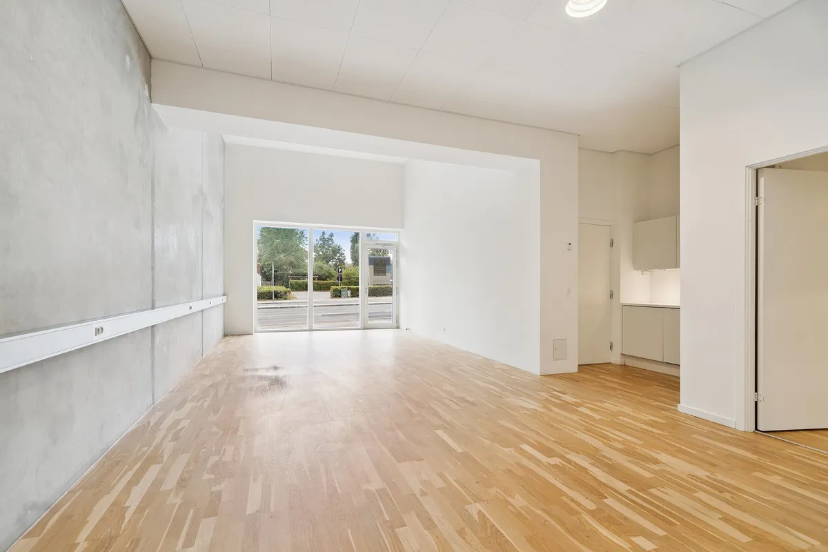 Et tomt kontor med lyse gulv og vægge samt et smukt glasdør- og vinduesanlæg samt en indgang til en køkkenafdeling