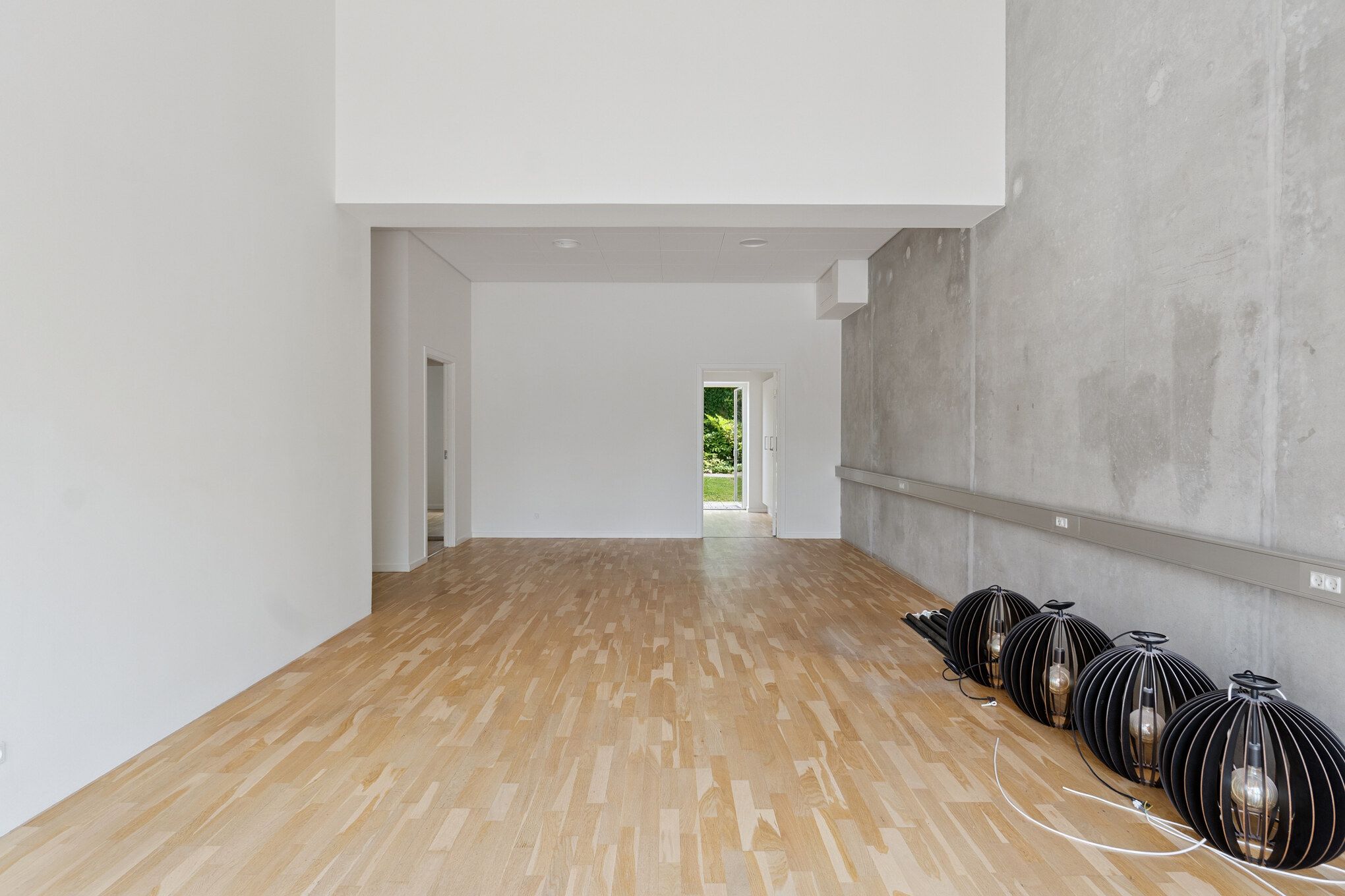Et stort lyse interiør med blanke gulvplanker, hvide vægge og en stærkt tekstureret grå væg med et elektrisk stik og fire lysekroner