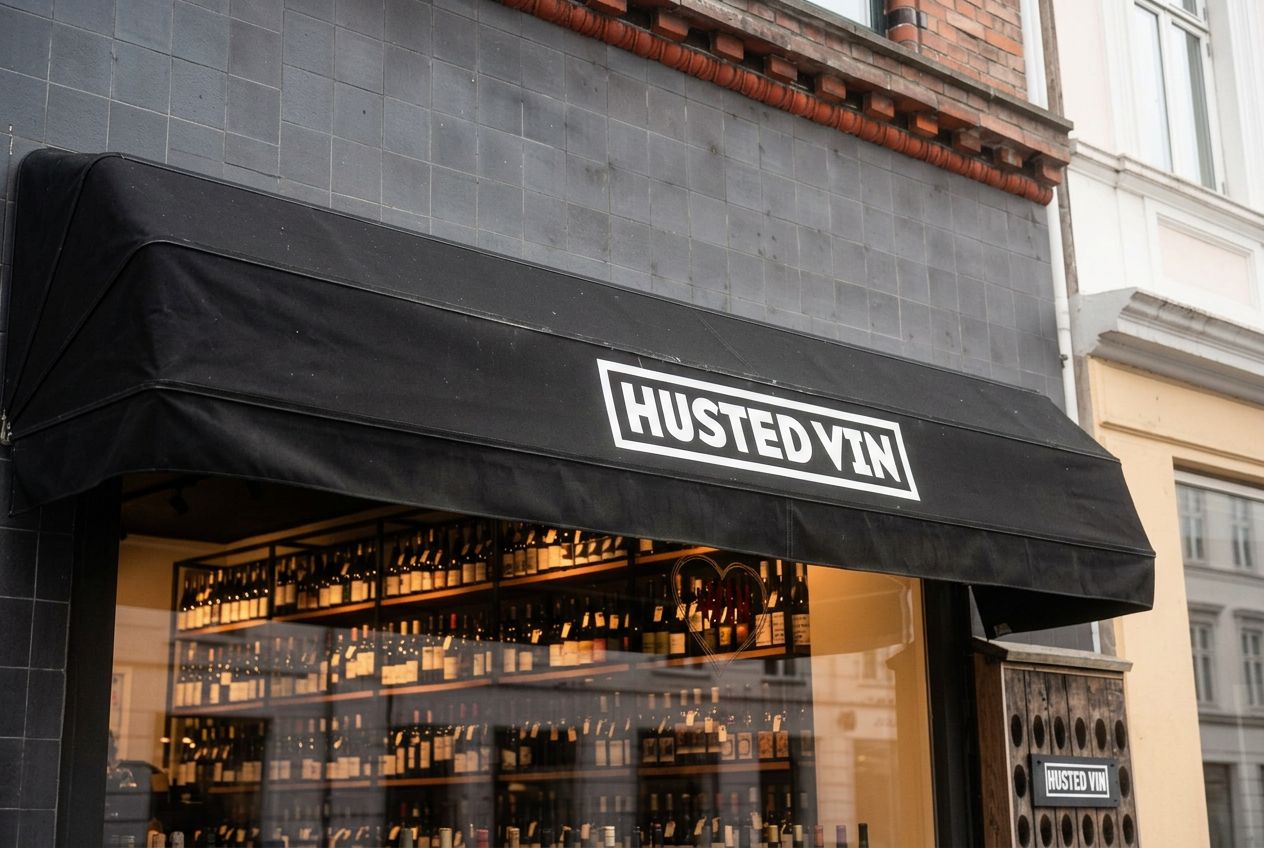 Husted Vin-butik med sort telt og udsigt til mange vinflasker i hylder i vindue. Bygningen er teglklædt og er på Nordre Frihavnsgade i København.