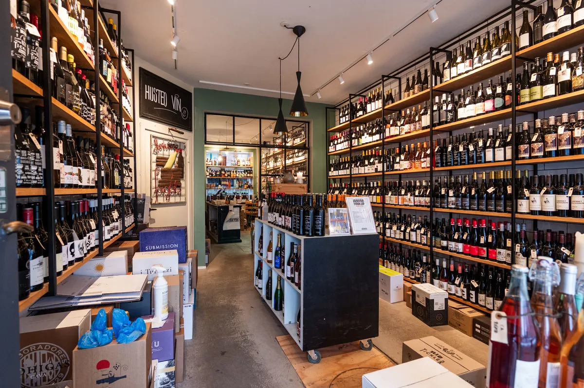 Butik med store hylder og skraldespande fyldt med vinflasker og etiketter samt kassevogn og flere kasselag.