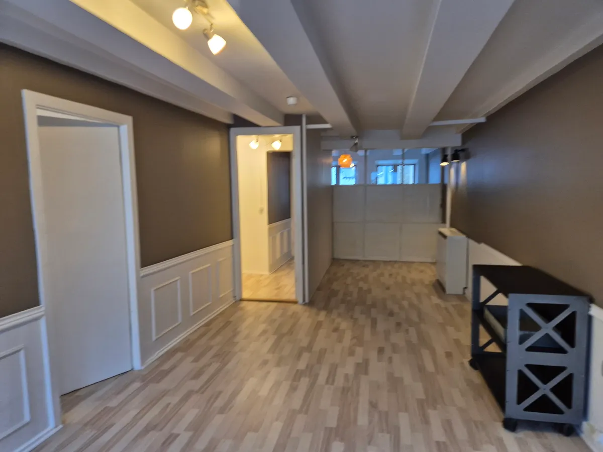 Kontorlokalt på Rådhusstræde 11 med hvide vægge og trægulv. Vægpaneler og åbne døre mod korridor. Møbler og belysning i loftet.