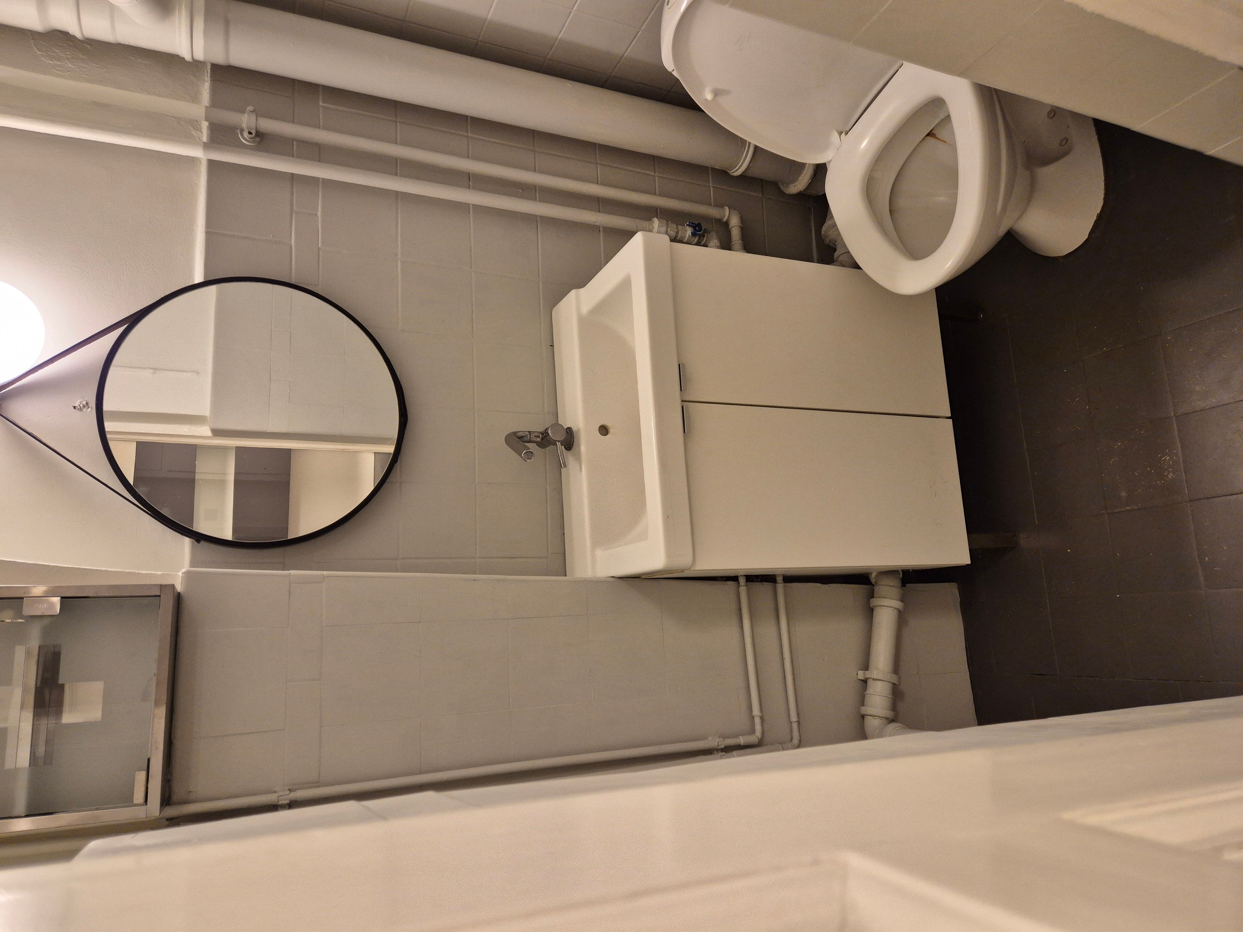 Et moderne badeværelse med et hvidt toilet, spejl og hvidt underskab med vandhaner samt lyse og lyserøde vægge.