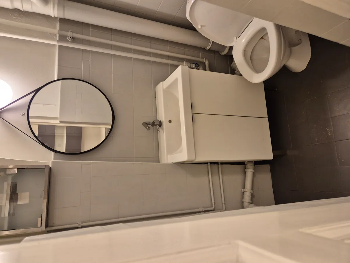 Et moderne badeværelse med et hvidt toilet, spejl og hvidt underskab med vandhaner samt lyse og lyserøde vægge.