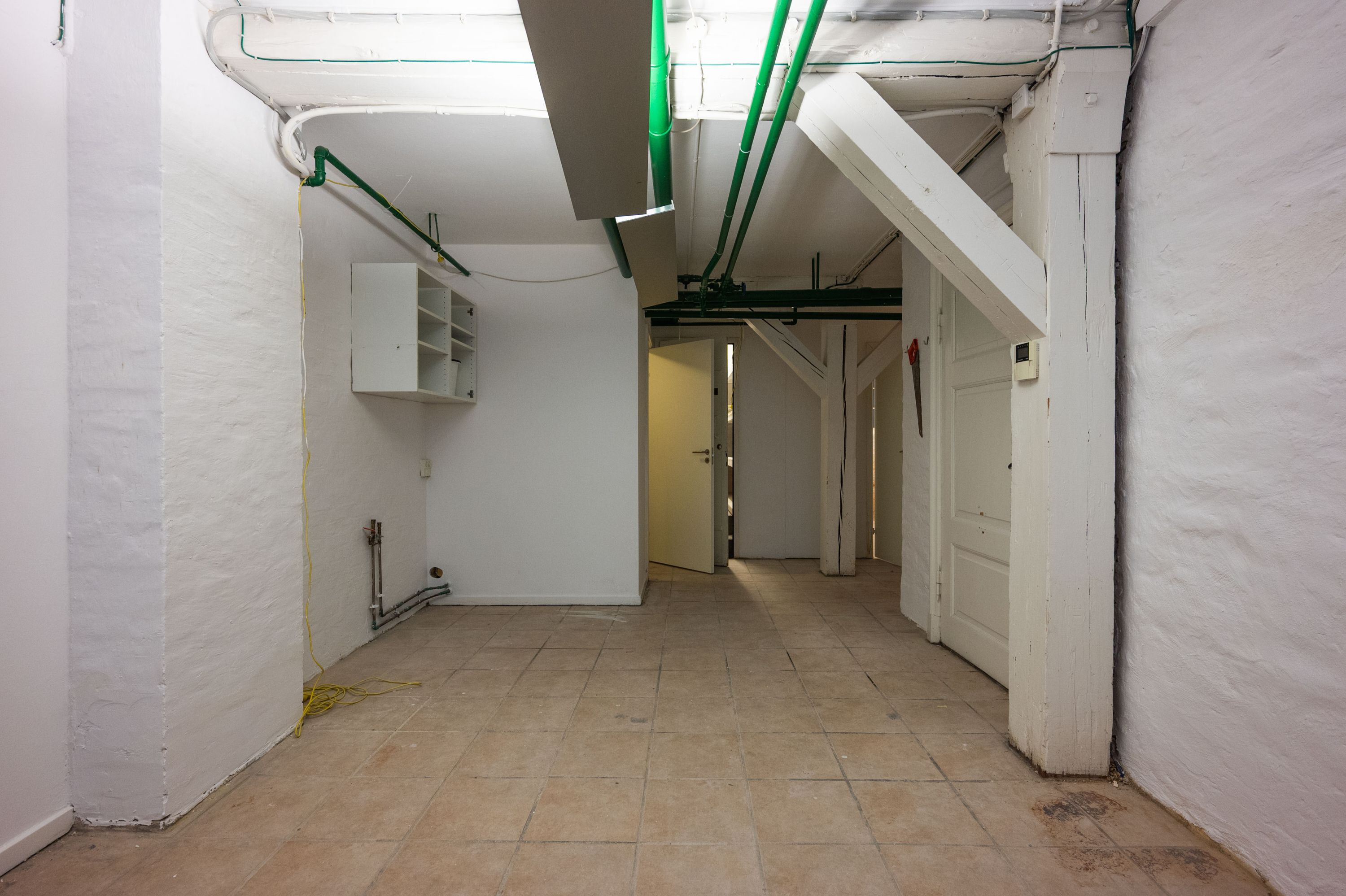 Lej et værksted med højloft og lyse gulve i Københavns kvarterer. Bygningen har flere døre og en højloftet kælder med flere funktioner.