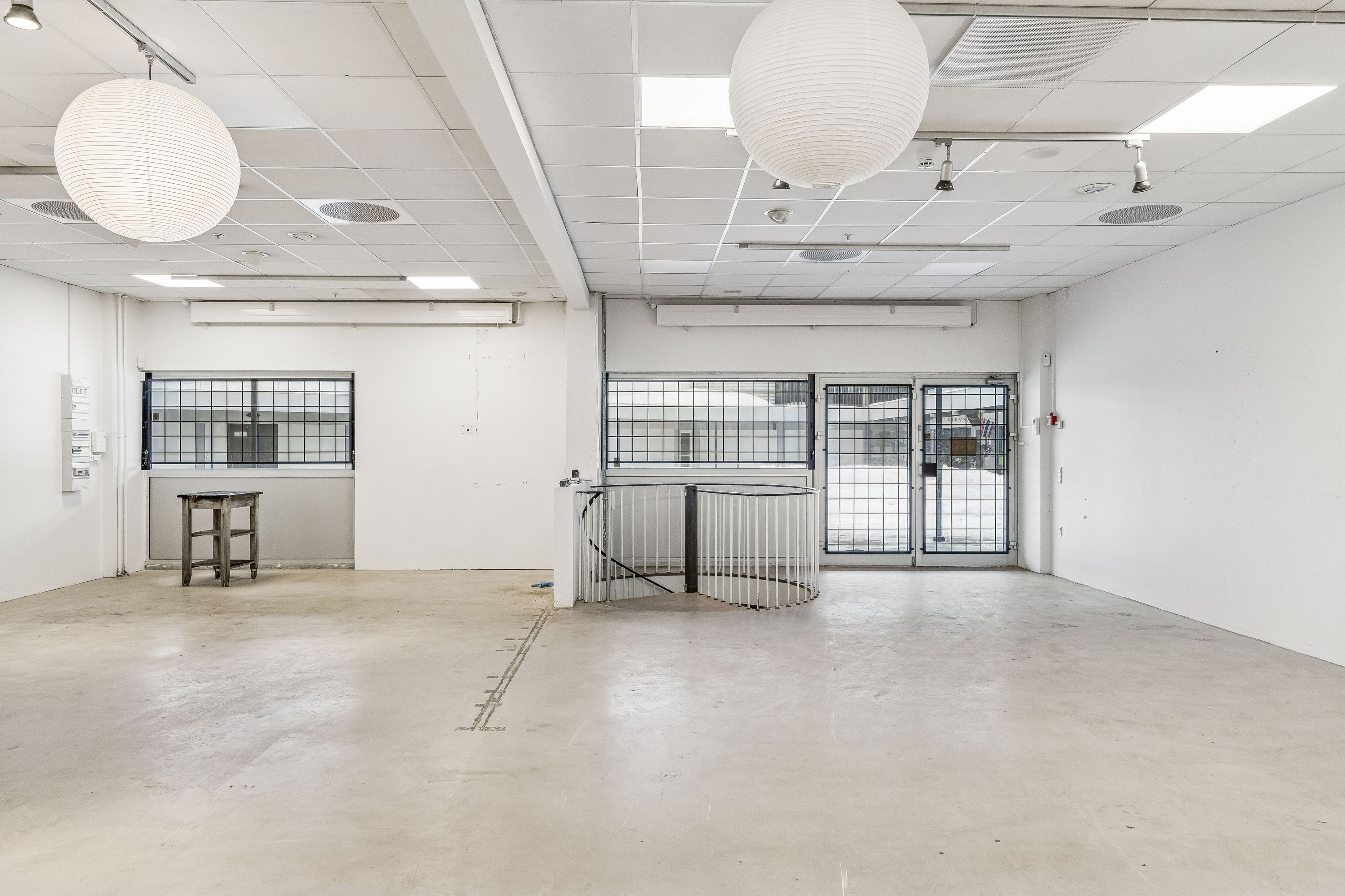 Store, hvide butikslokaler med glasruder og hvide vægge samt lysekroner og et højt loft med runde loftsventiler og et snoet trappeværk