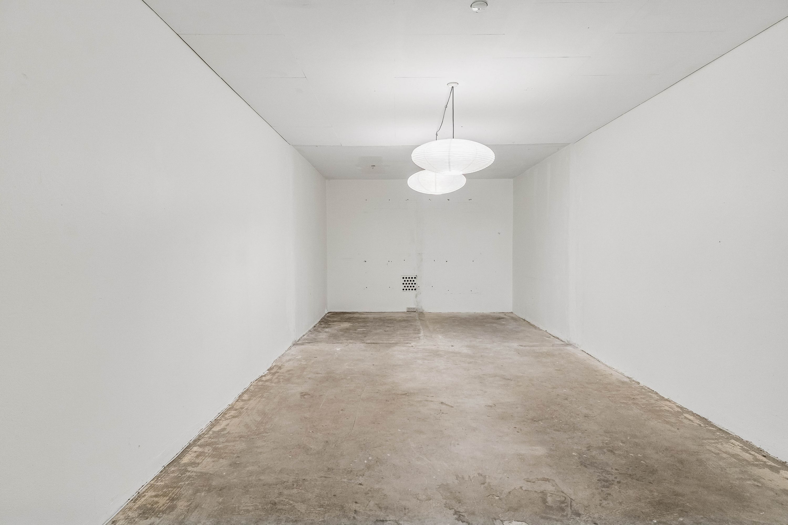En tom og mørk butik med hvide vægge og loft. To hvide runde lamper hænger fra loftet. Gulvet er mørt og ubehandlet