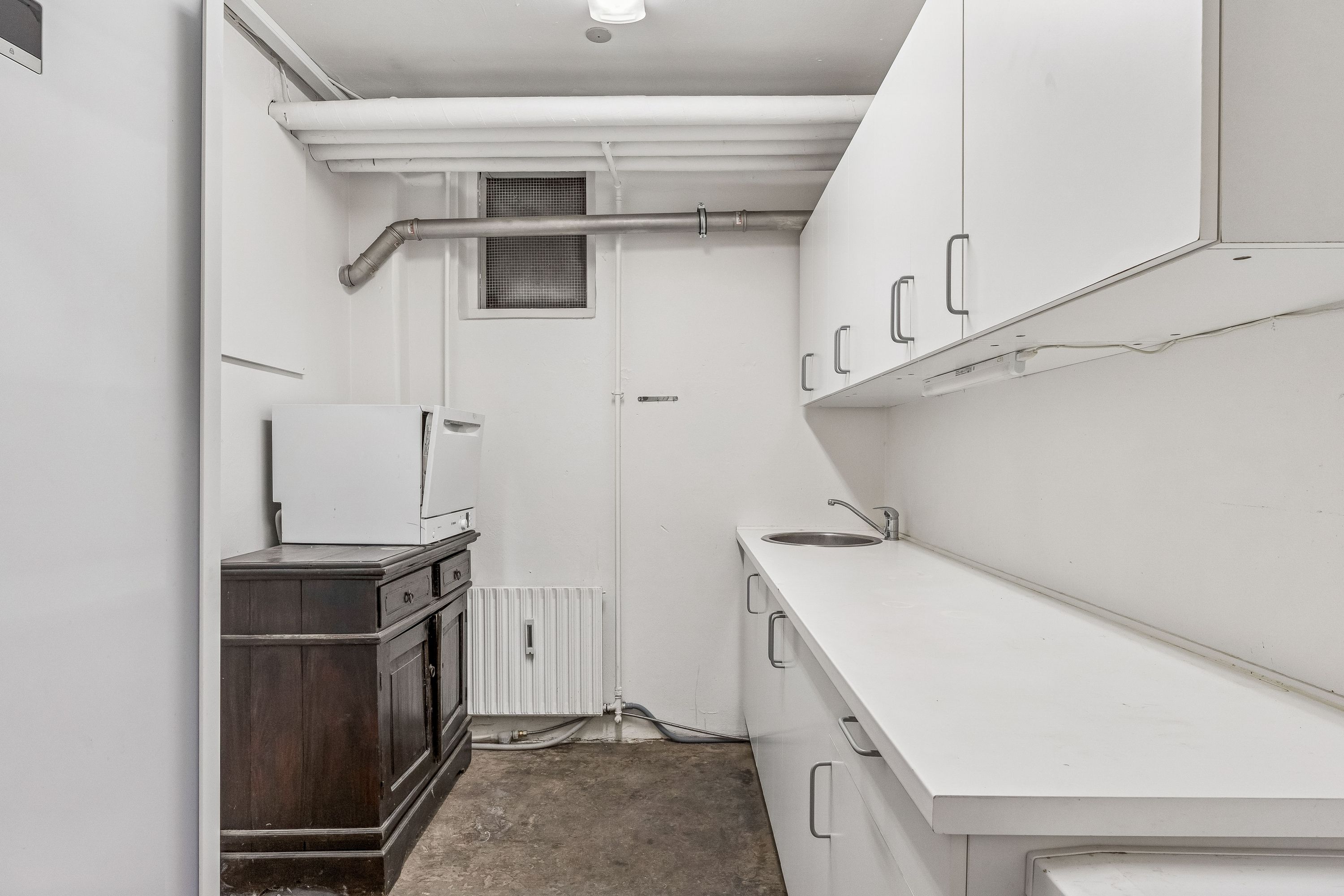 Moderne køkken med hvide vægge og lyse lofter hvor et hvidt komfur og en hængende lampe sammen med en sænket sæde og en sænket vandhaner og et hvidt køkkenbord