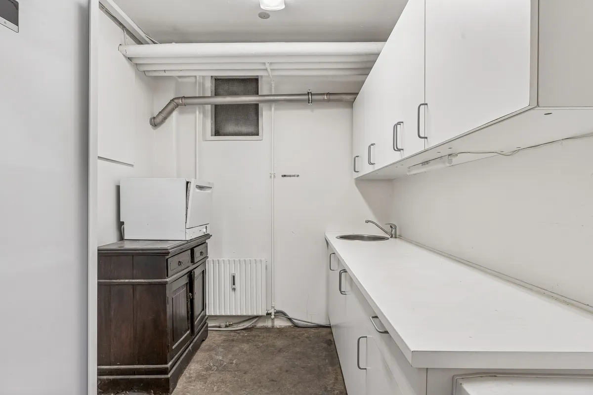 Moderne køkken med hvide vægge og lyse lofter hvor et hvidt komfur og en hængende lampe sammen med en sænket sæde og en sænket vandhaner og et hvidt køkkenbord