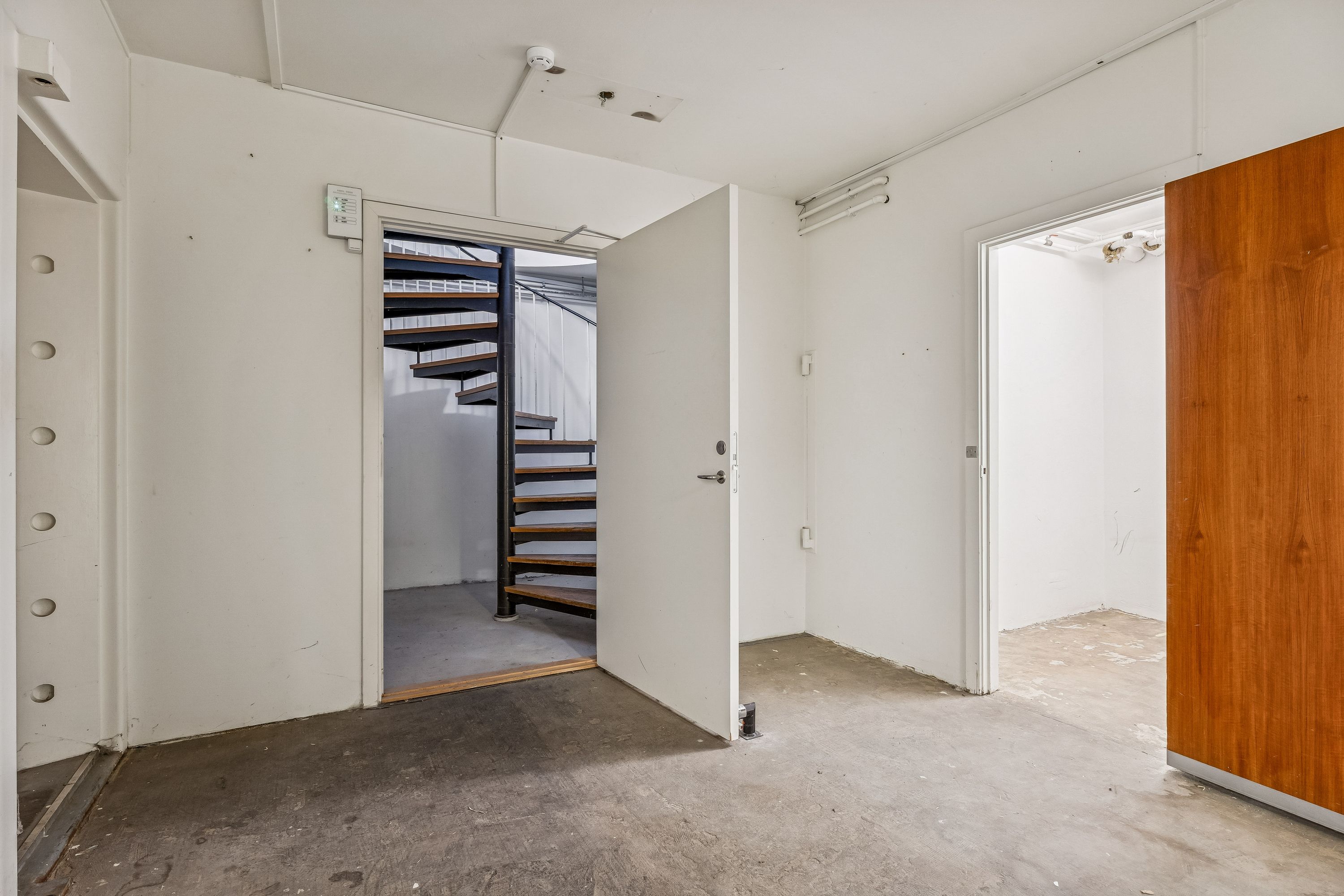 Tomt rum med åben dør til kælder og trappe. Dekorative hængebolte og et indbygget sikringsskab. Større rum med åbne døre til venstre og højre