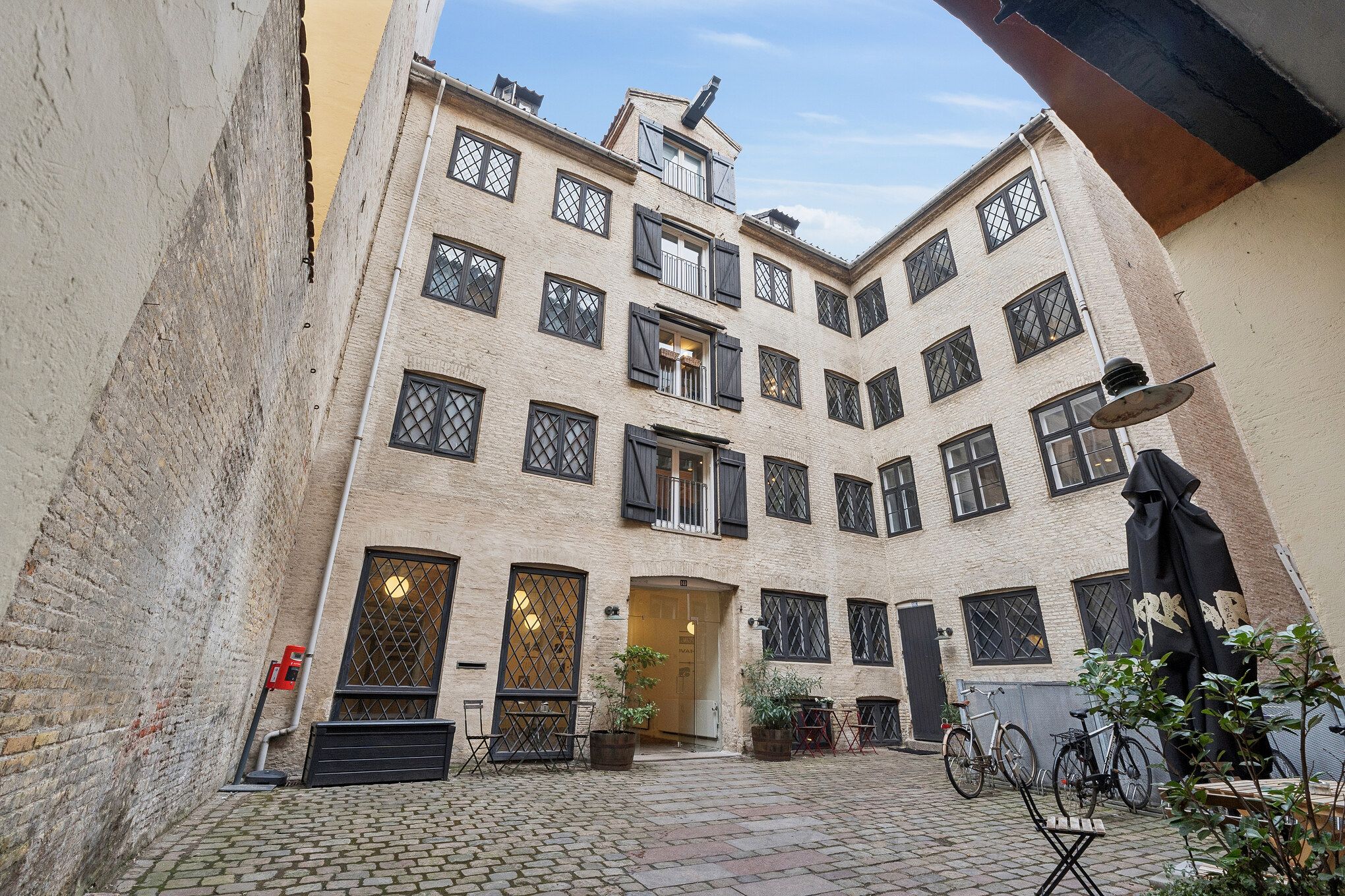 Kontorbygning med flere etager og mange vinduer samt to cykler parkeret på gårdspladsen og en lukket parasol