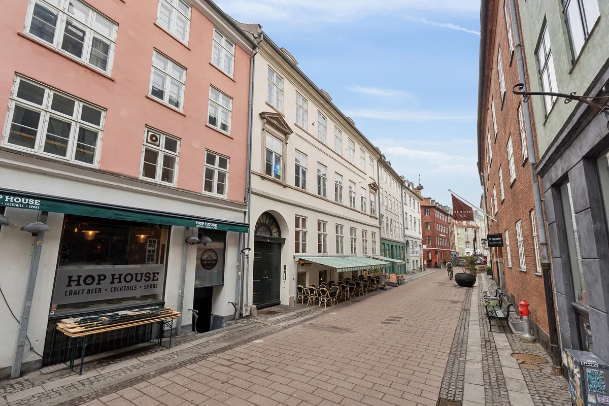 Strædet i København med tomt hjørne og butikslokaler med grønne facader og solskærme samt to røde brandvandsslanger og en rødmalet søjle i bakgrunden