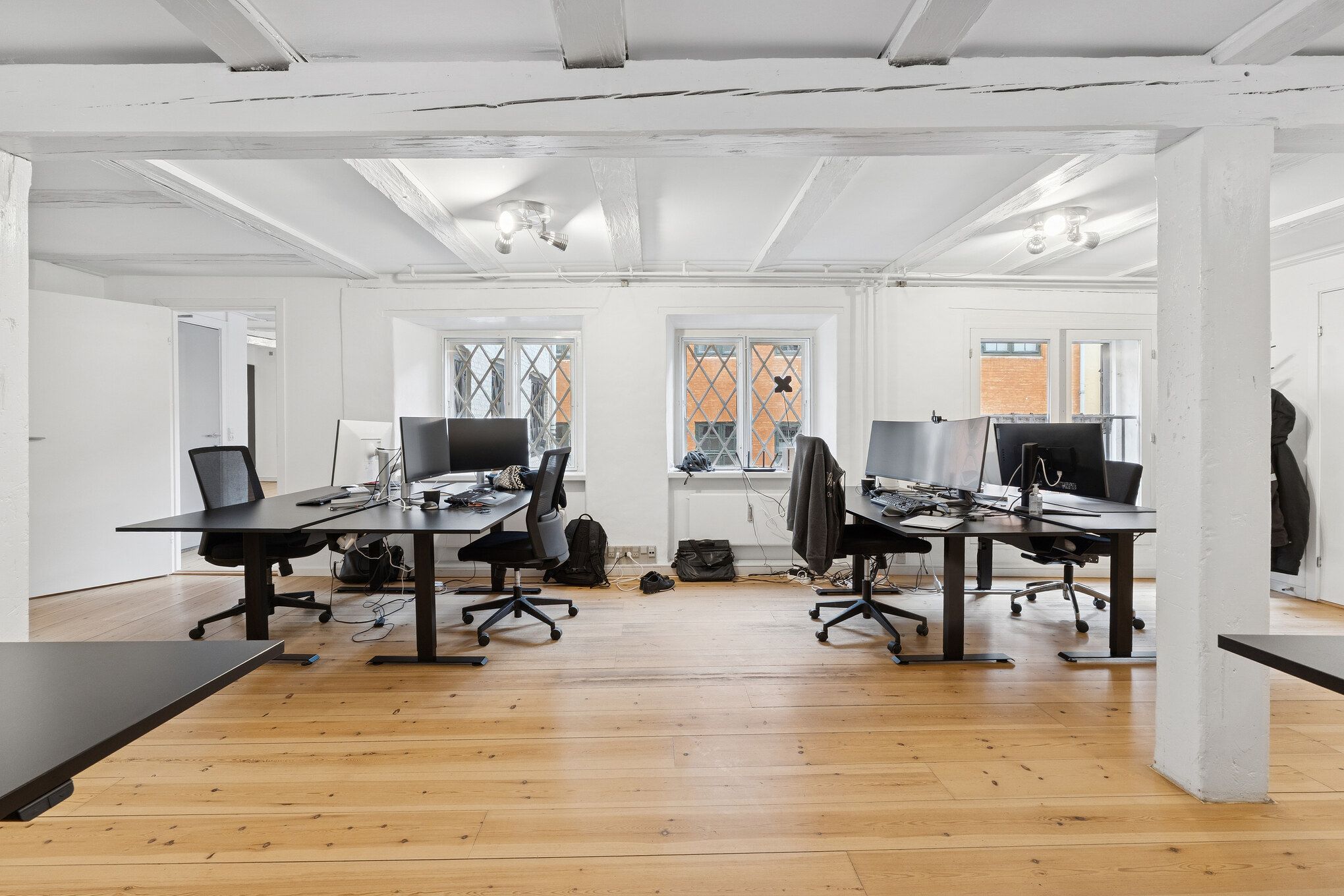 Kontorrum med lyse lofter, moderne møbler, computere og skriveborde, alle fordelt i et stilrent og renset miljø med trægulve