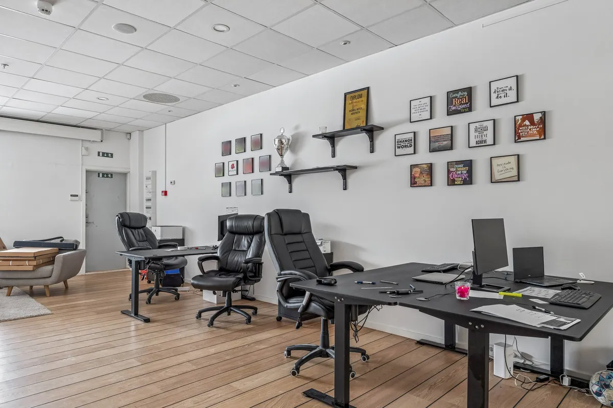 Billede af et moderne kontor med smukke trægulve, lyse vægge og flere kontormøbler. To ergonomiske stole og to store skriveborde er udstyret med computere og skriveartikler.