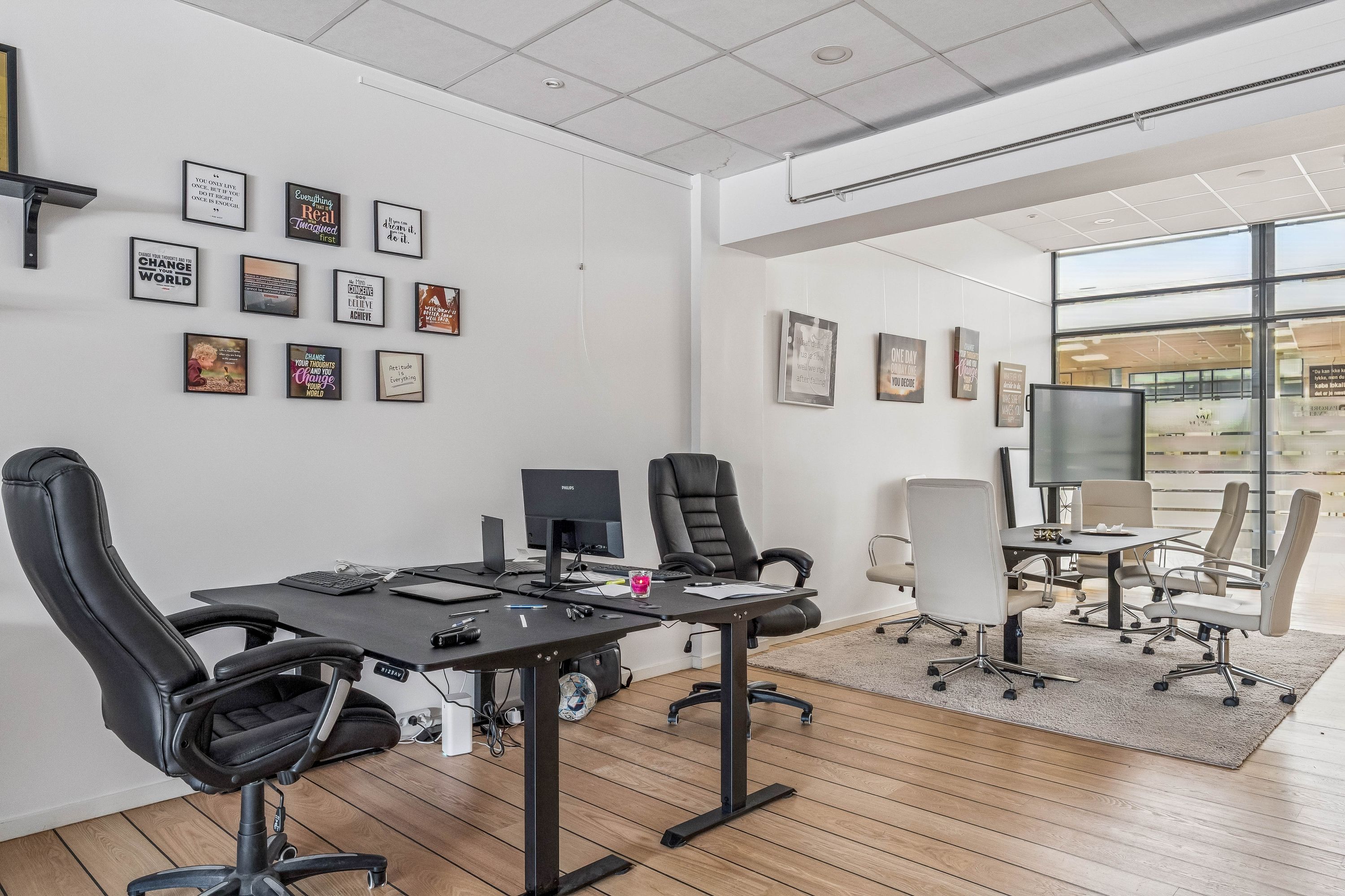 Kontor med to borde og computere, stolpe med indskrifter og billeder, tv, ståbord og konferencebord samt tekst "Change the world" på væggen.
