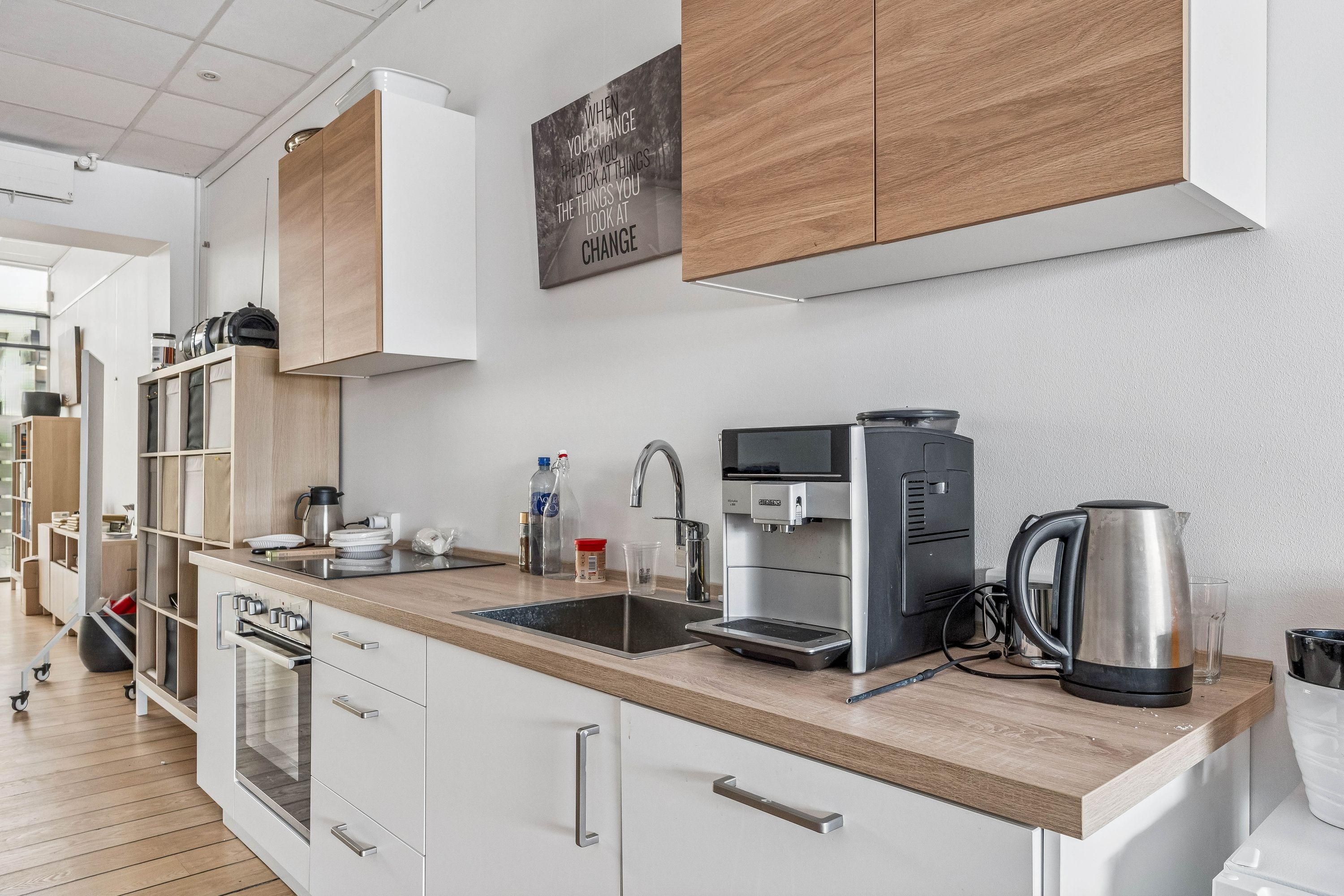 Reglerig og velindrettet køkken med moderne udstyr, højt loft og lyst gulv. Køkken med hvide skabe, brændenælde, kedel, ovn og køleskab. Møbler og apparater i moderne stil