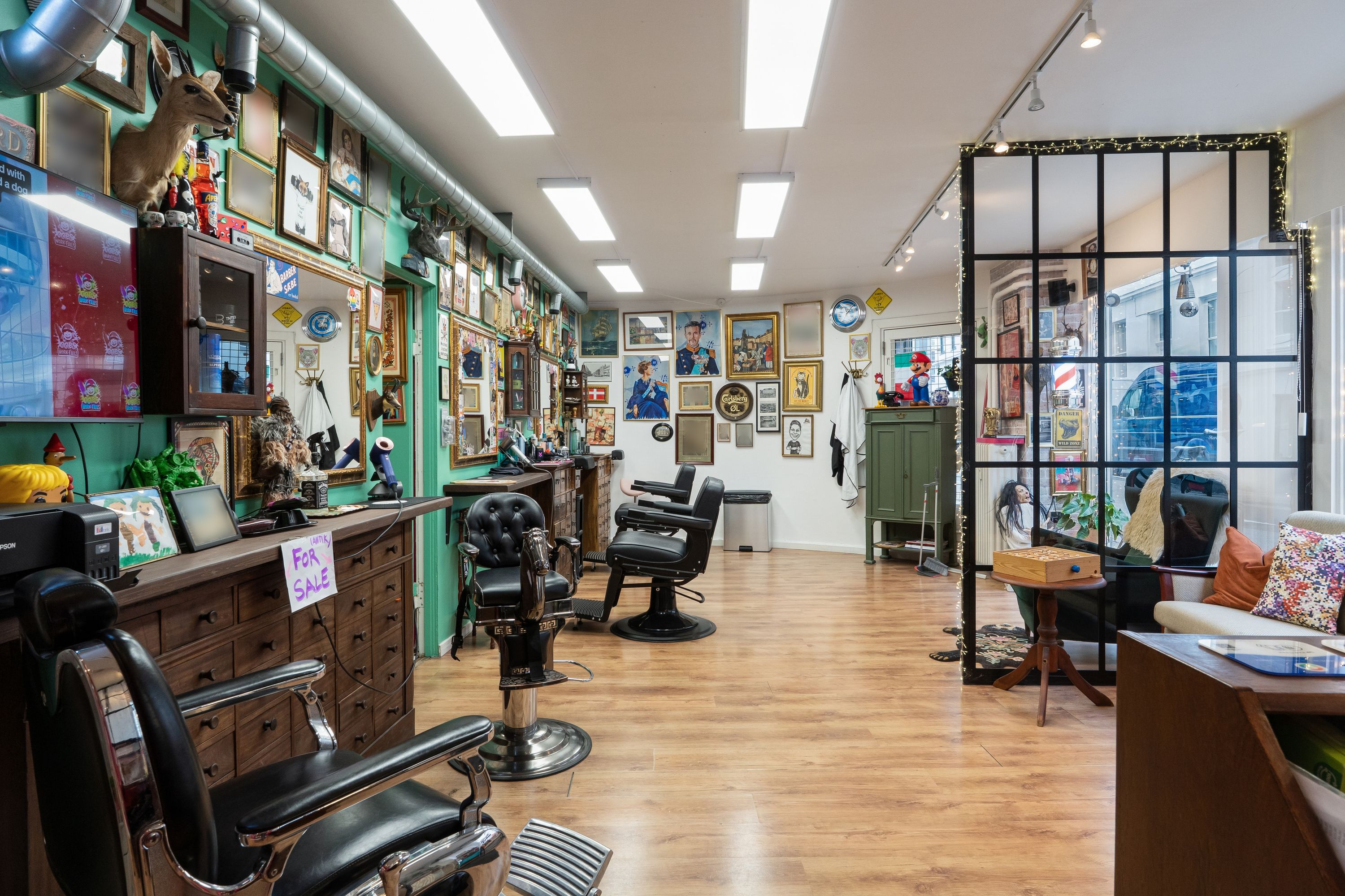 Barberforretning med barberstole og udsmykning i lokalet med grønne vægge og lysekroner med lyseperler i loftet