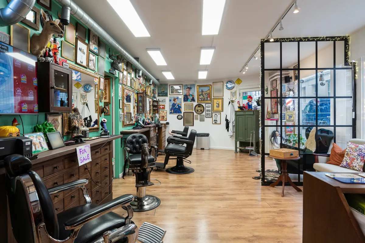 Barberforretning med barberstole og udsmykning i lokalet med grønne vægge og lysekroner med lyseperler i loftet