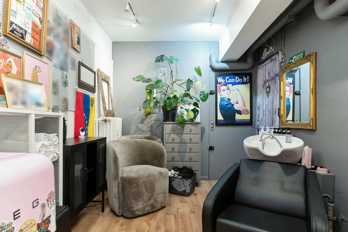 En skøn interiør med plante, to stole, et hårklippestol, et spejl og en håndvask med toiletartikler.