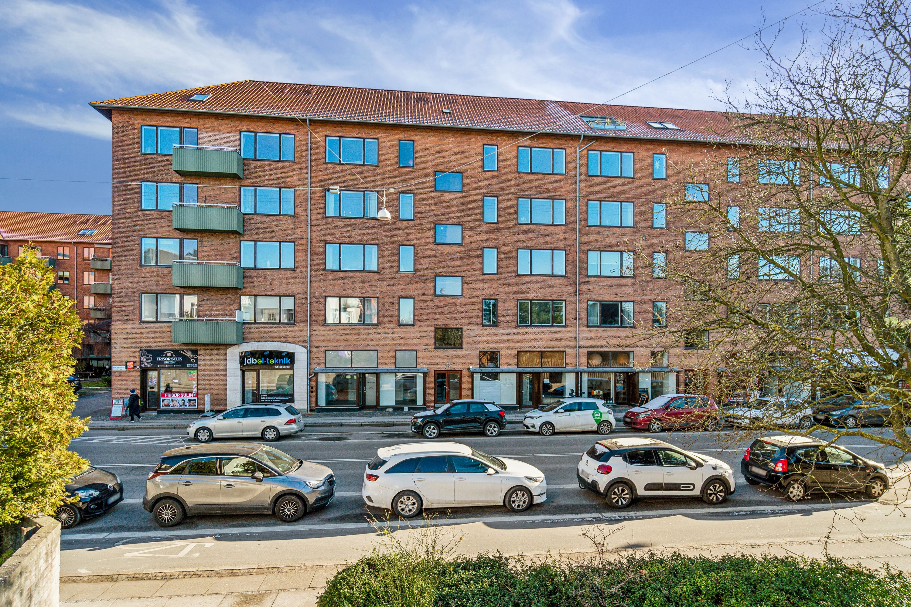 Erhvervslokale til leje på Søndre Fasanvej 45 i Frederiksberg med mange biler parkeret udenfor og butikker og en kontorvæg i første række