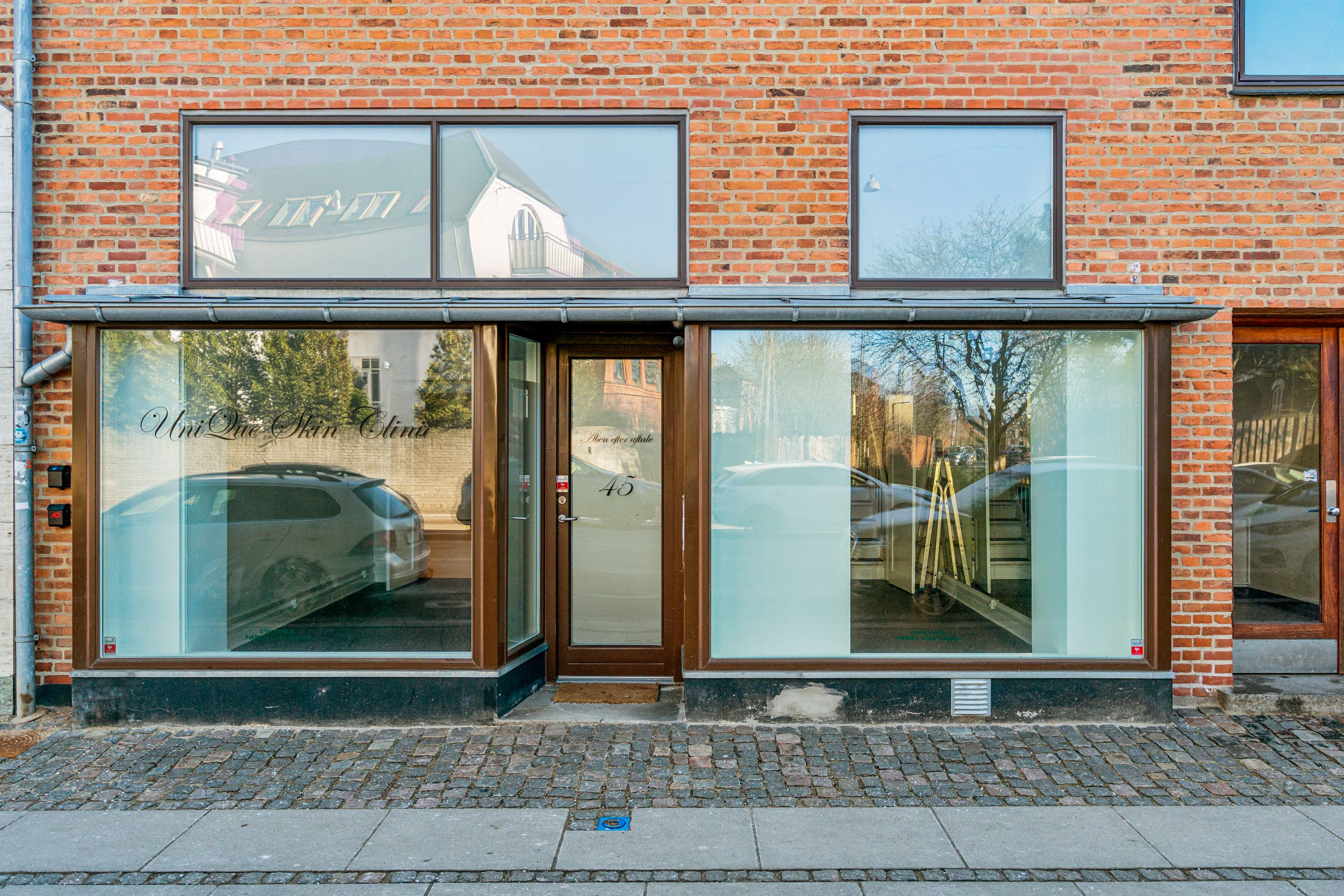 Butik til leje på Søndre Fasanvej 45 i Frederiksberg med glasdøre og vinduer, refleksioner af biler og bygninger og et rødt nummer 45