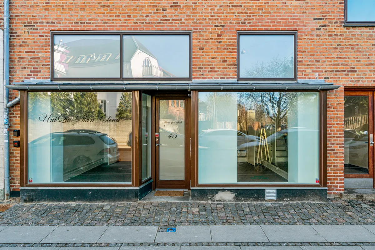 Butik til leje på Søndre Fasanvej 45 i Frederiksberg med glasdøre og vinduer, refleksioner af biler og bygninger og et rødt nummer 45